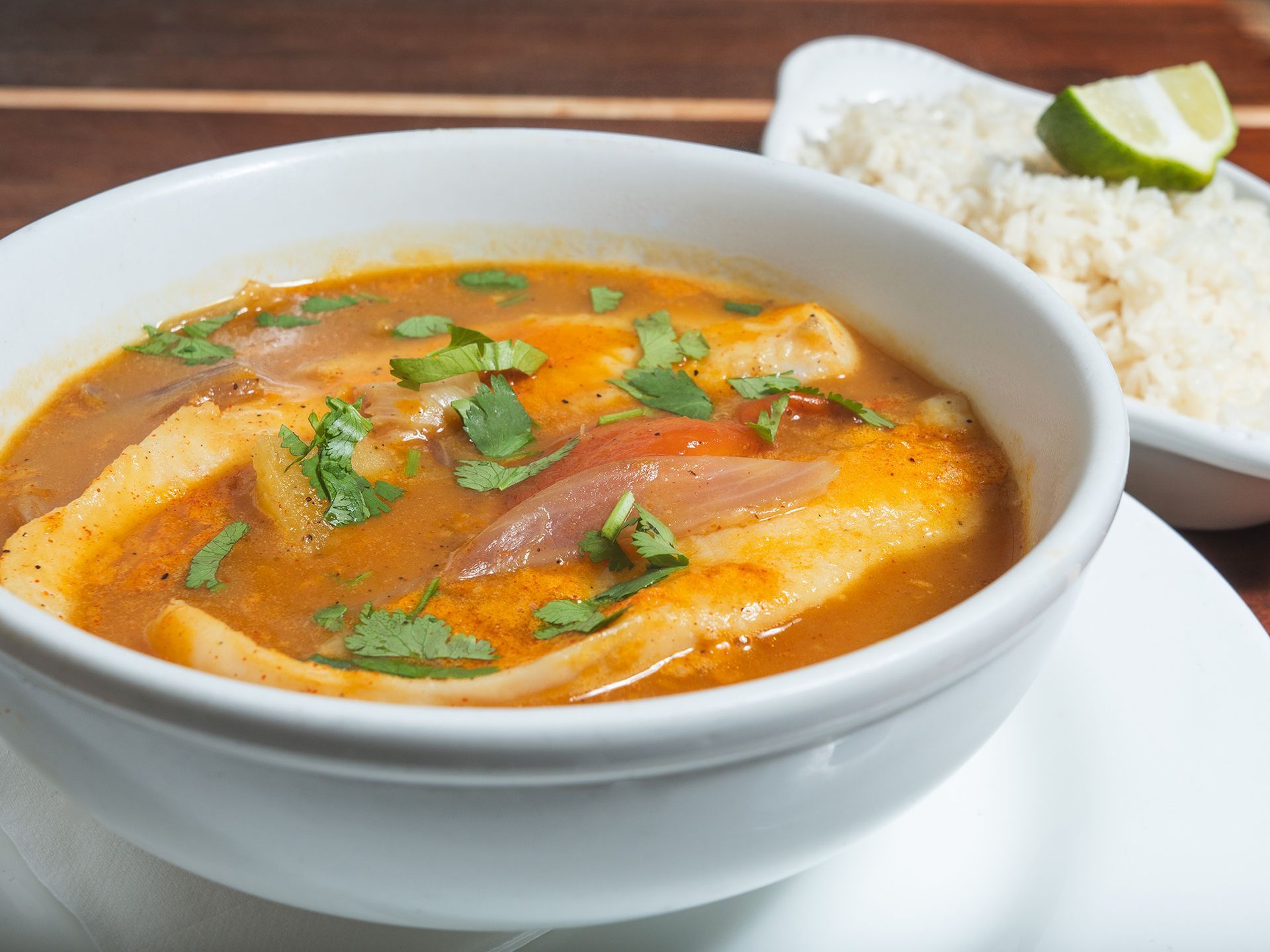 Bowl of stew with fish, onions, and cilantro, served with rice and a lime wedge.