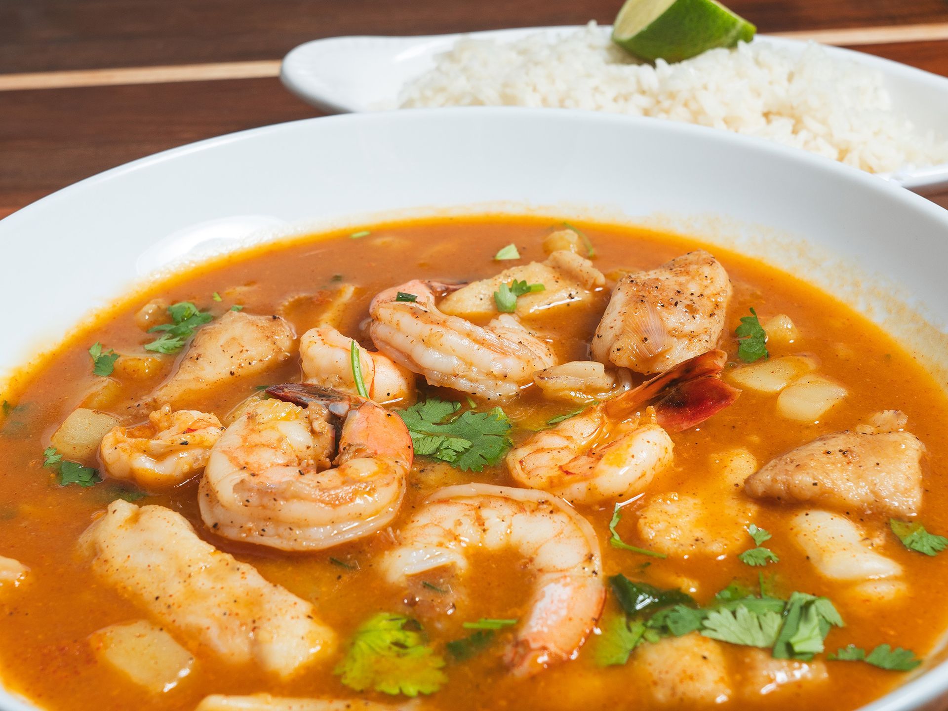 Seafood stew with shrimp and fish, garnished with cilantro; rice and lime in the background.