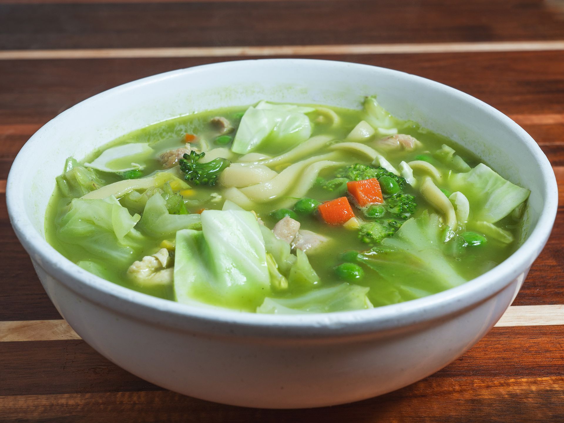 Bowl of green vegetable soup with noodles, cabbage, broccoli, and carrots.
