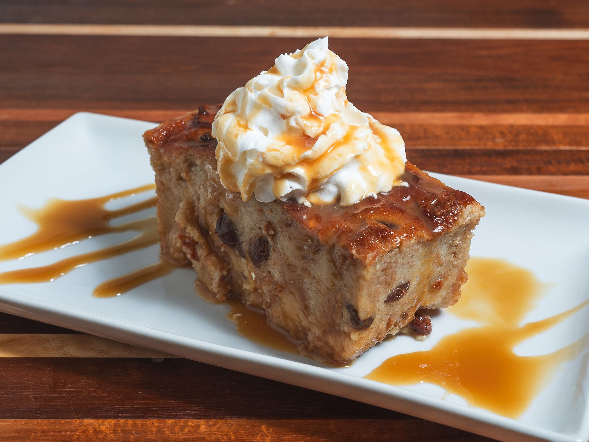 Bread pudding with whipped cream and caramel sauce on a white plate.