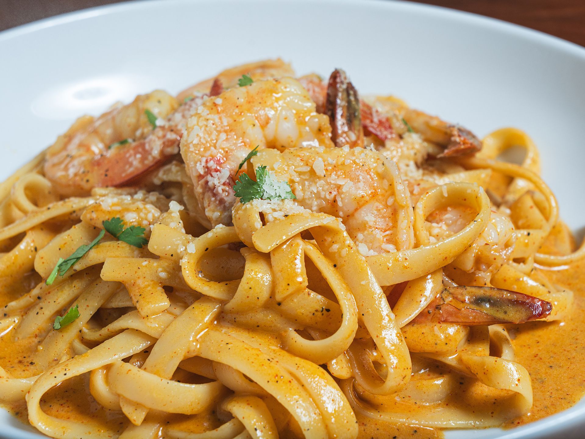 Fettuccine pasta with creamy orange sauce, shrimp, and grated cheese in a white bowl.