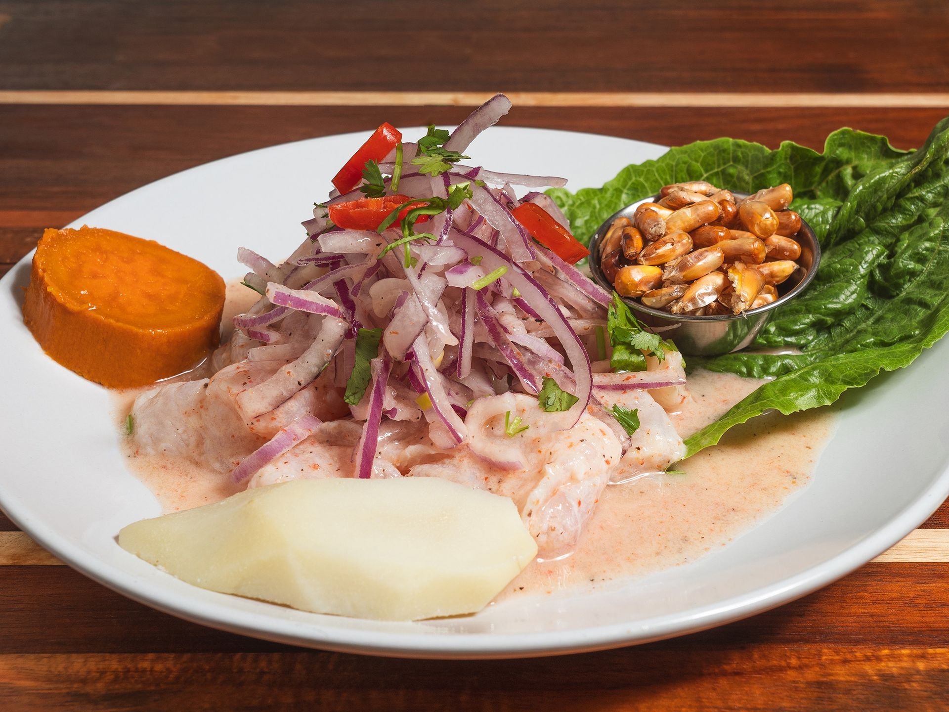 Ceviche dish on a white plate with sweet potato, corn, lettuce, and red onion.