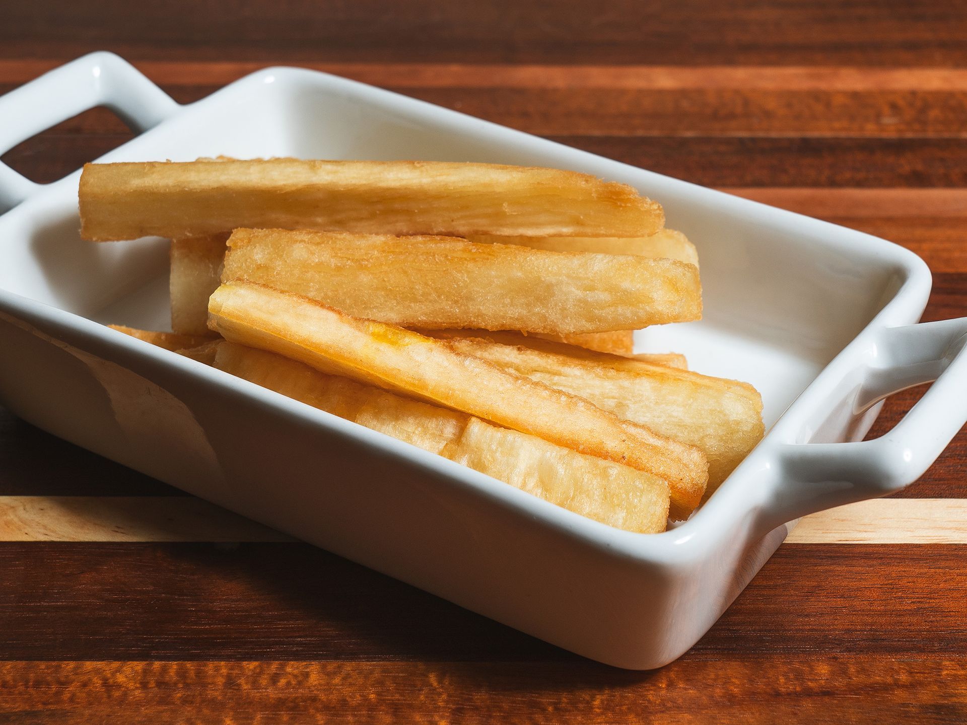 Fried yucca in a white serving dish on a wooden surface.