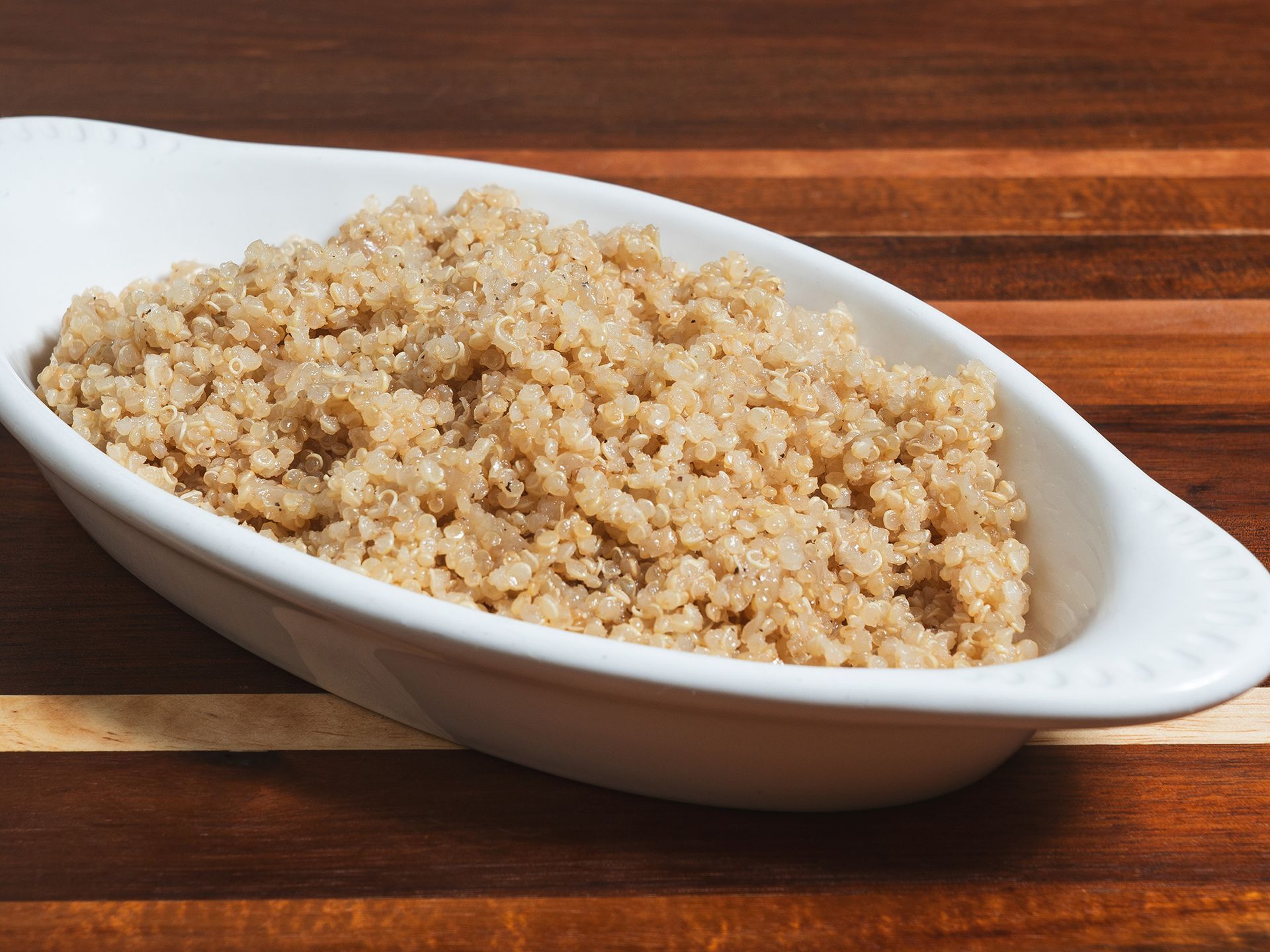Cooked quinoa in a white oval dish on a wooden surface.