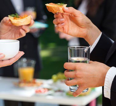 People in suits holding appetizers and drinks at an outdoor gathering.