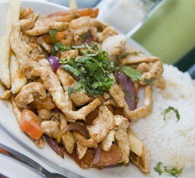 Chicken stir-fry with fries and rice, garnished with cilantro. Red onion and tomato visible.