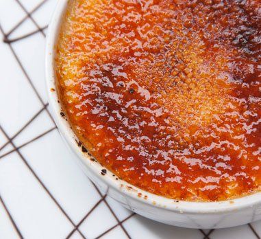 Crème brûlée with caramelized sugar crust in a white bowl on a geometric patterned surface.