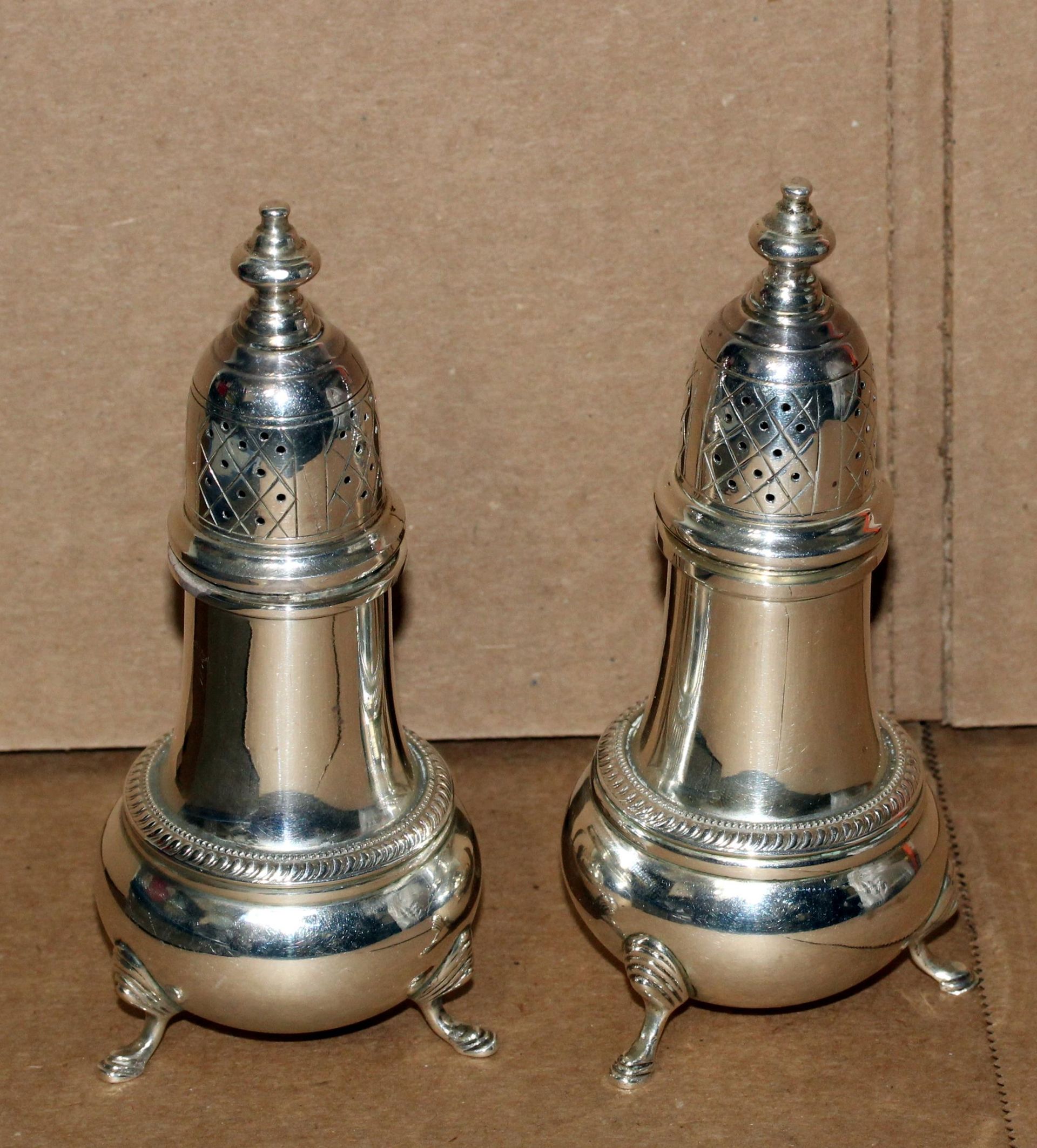 Two ornate silver salt and pepper shakers with domed lids and three feet.