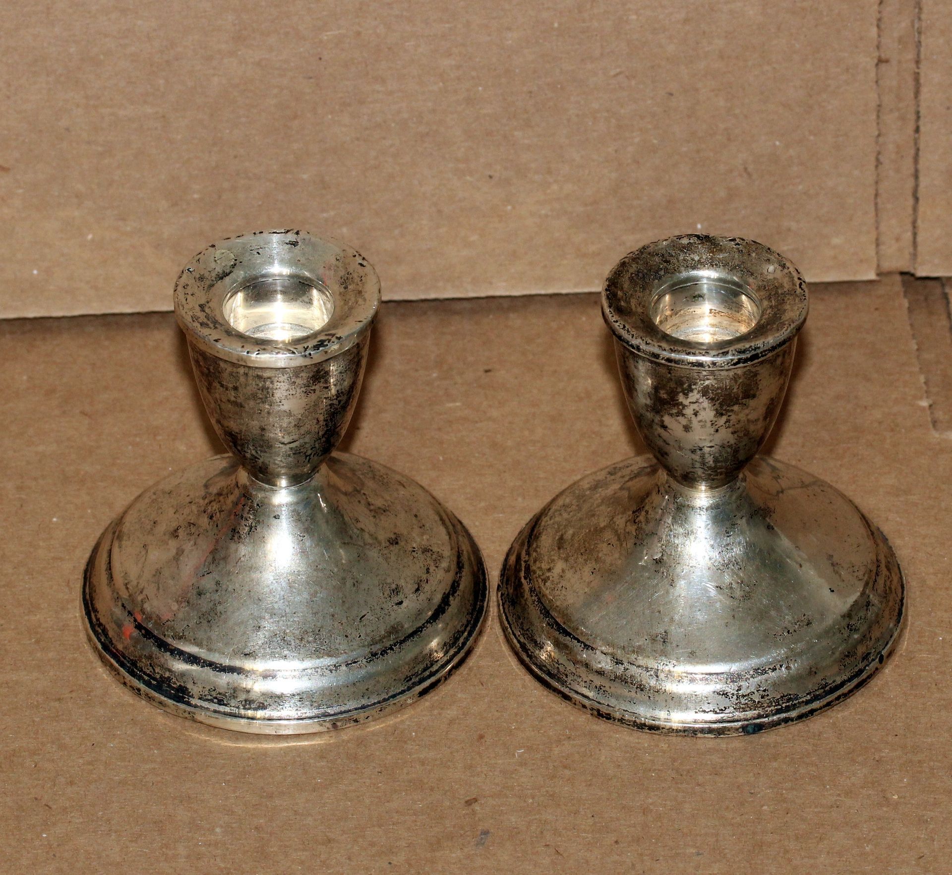 Two tarnished silver candle holders on a brown surface.
