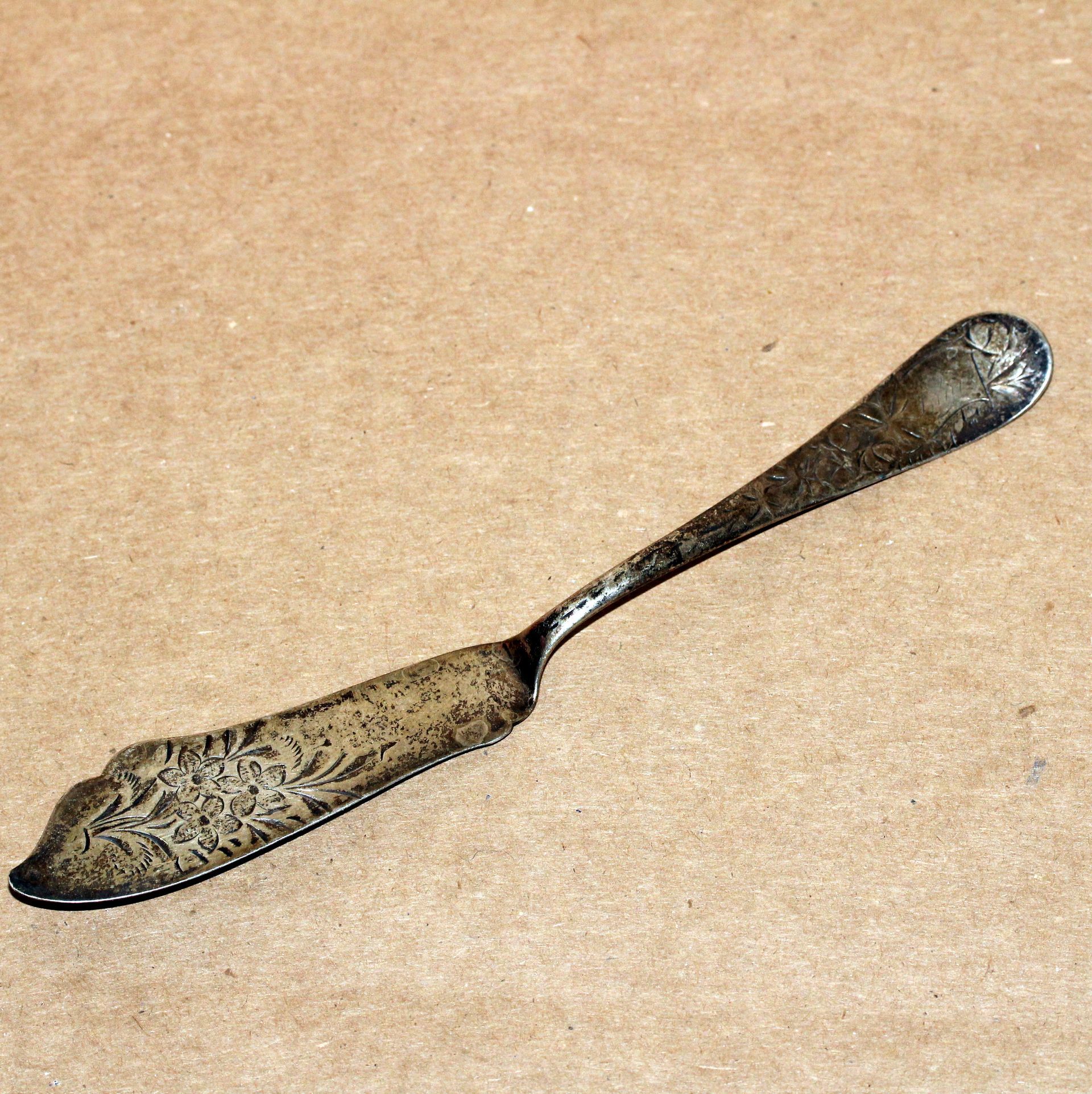 Silver butter knife with floral design on a brown surface.