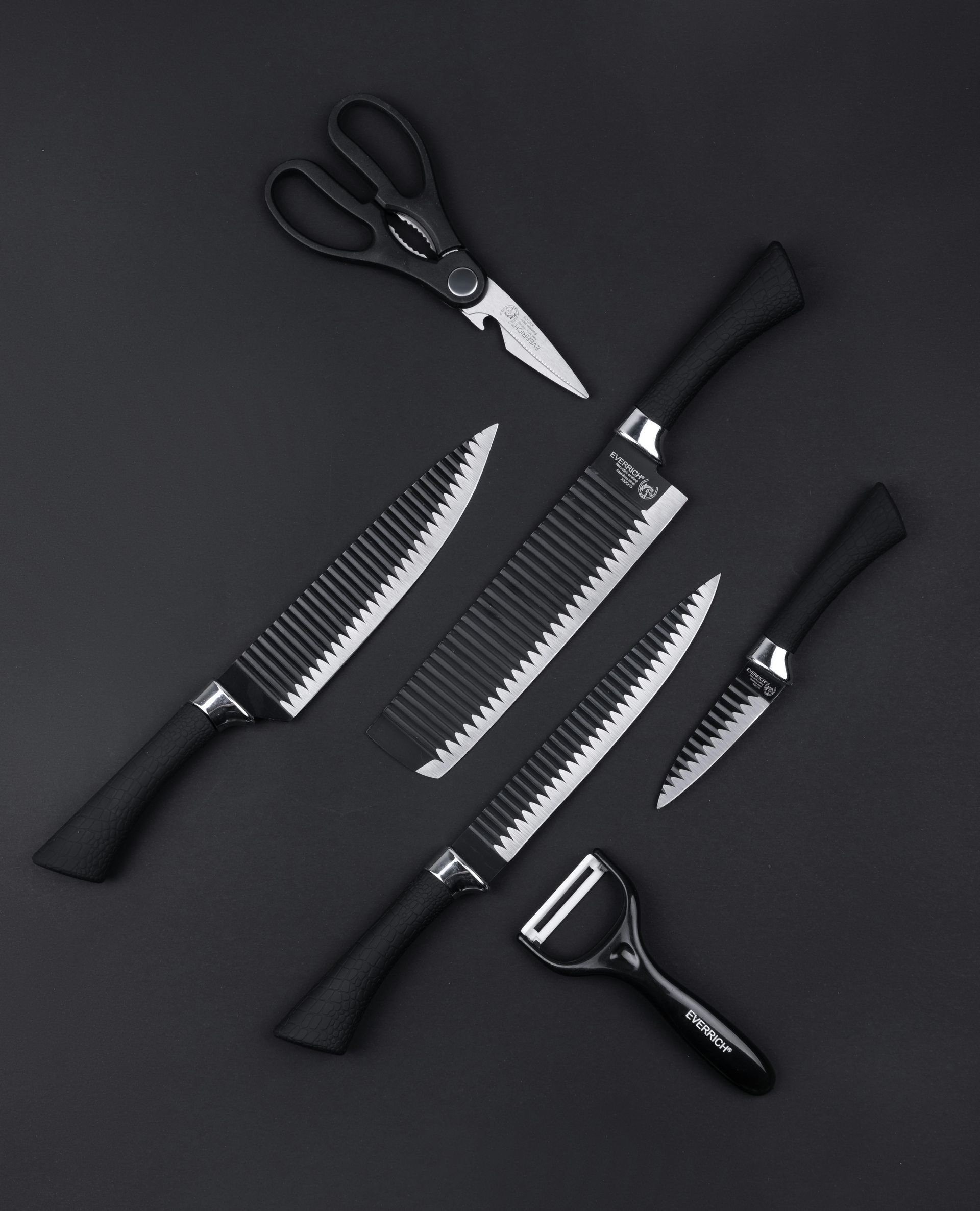 Black kitchen knives, shears, and peeler arranged on a black surface.