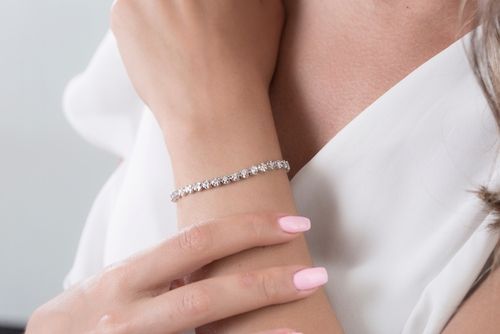 Woman wearing a silver bracelet with several clear stones, resting arm on another.