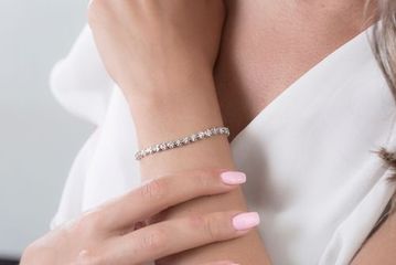 Woman wearing a silver bracelet with several clear stones, resting arm on another.