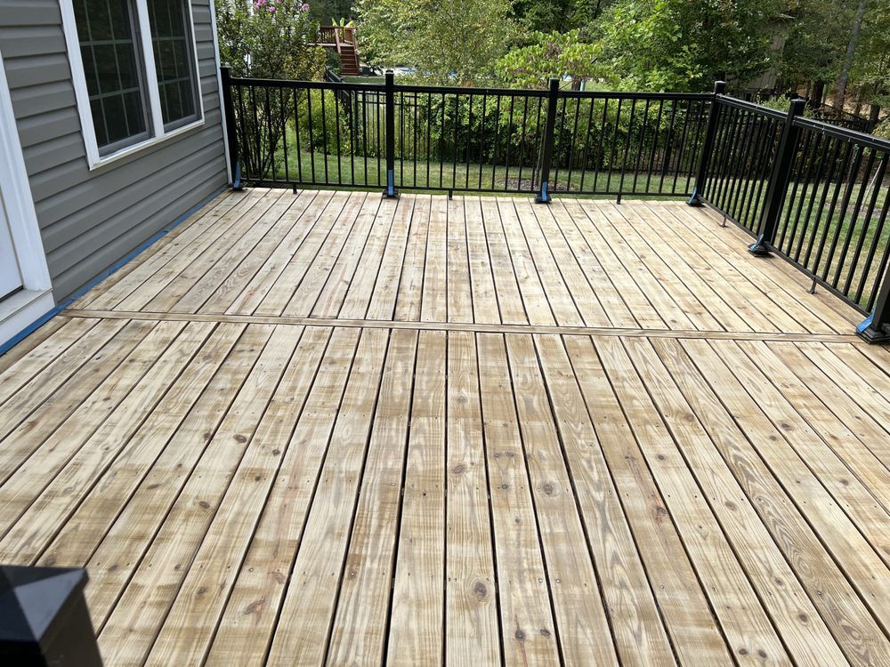 A large wooden deck with a black railing and a house in the background.