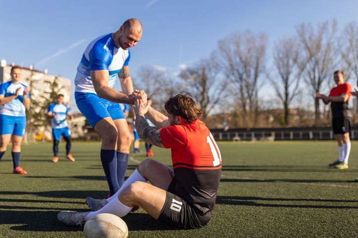 A medical professional examines a young man's knee. Indoors, white room, sunlight.