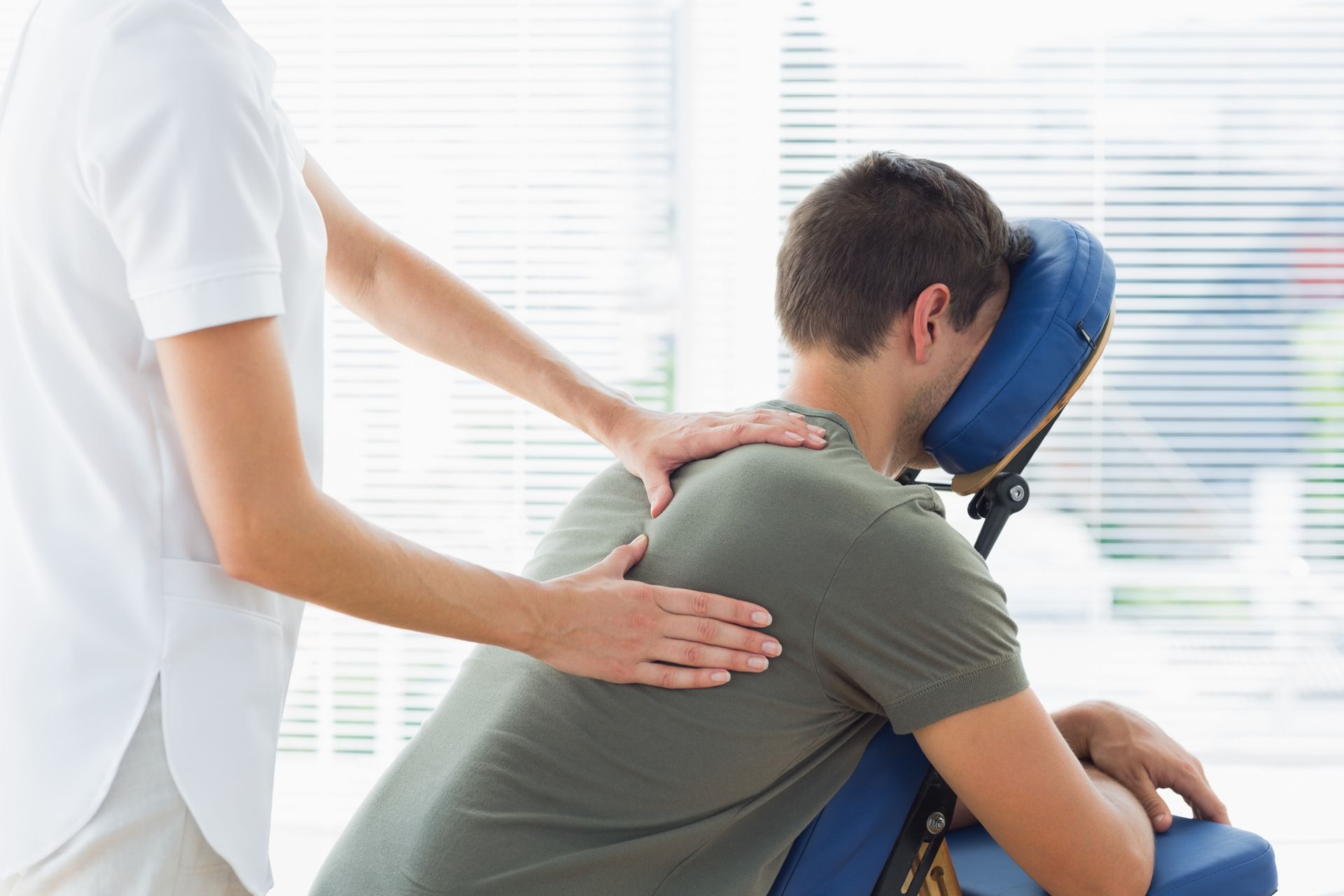 A person getting a massage on a blue massage chair. The masseuse is massaging their back.