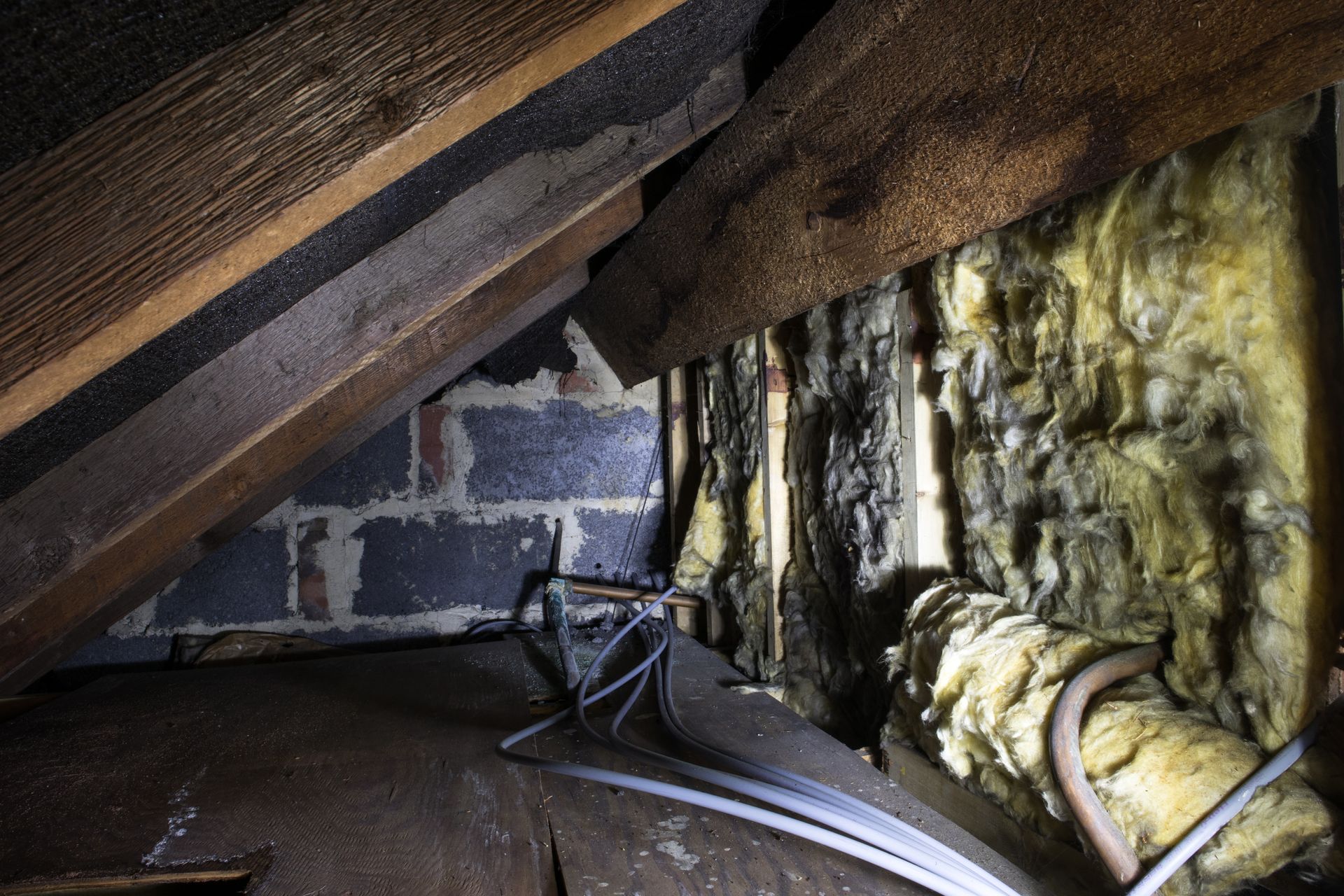 Crawl space with sloped rafters, exposed insulation, and a black cable or hose running along the floor