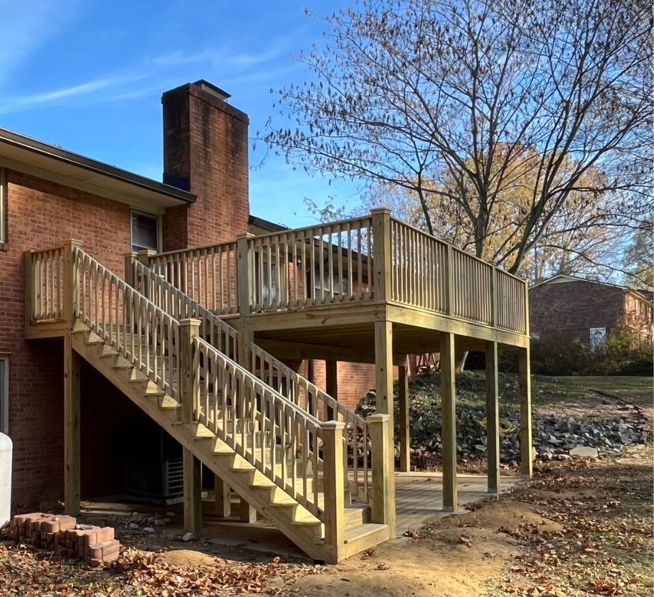 A wooden deck with stairs leading up to it is in front of a brick house.