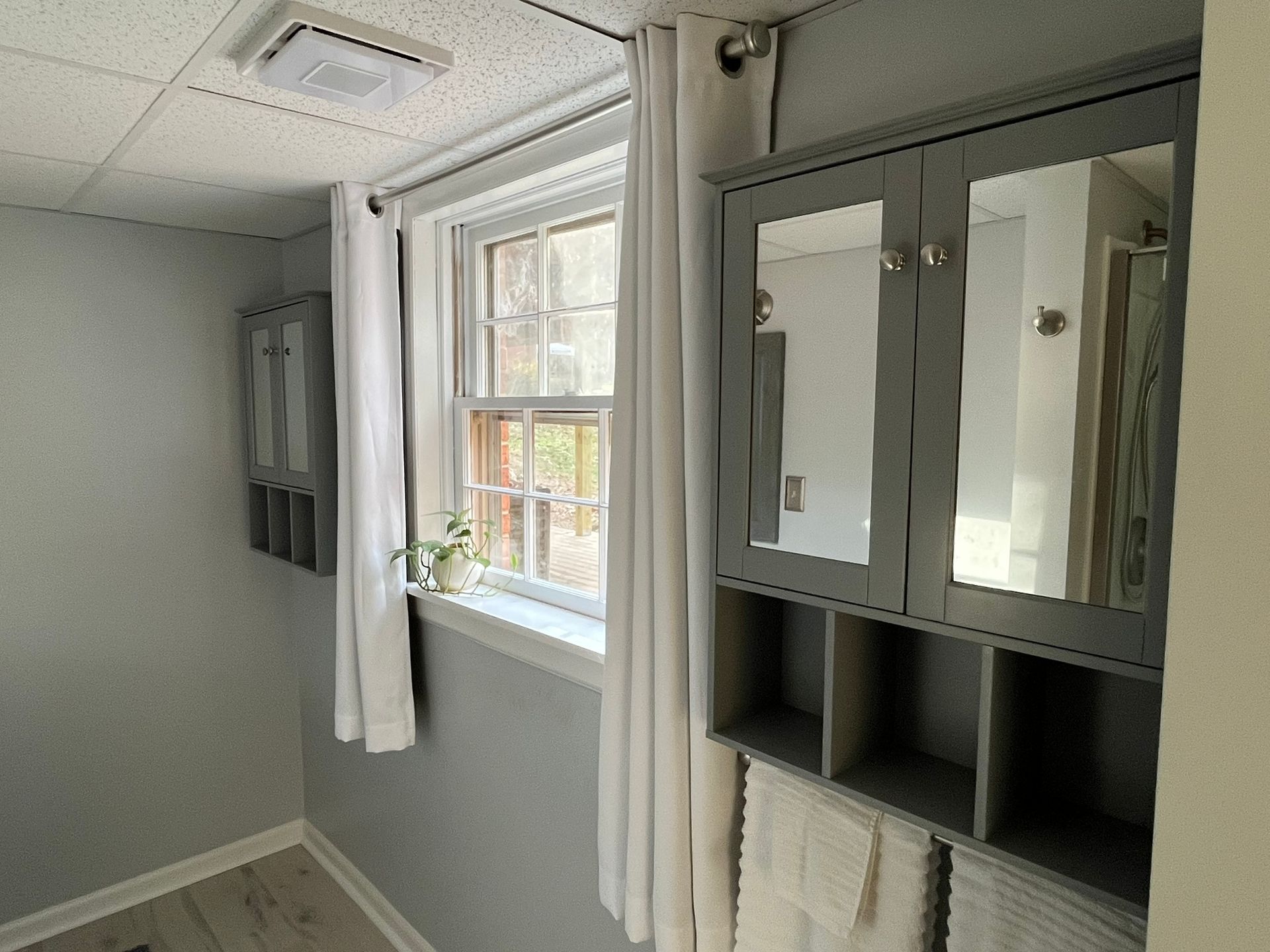 A bathroom with a window , cabinets , towels and mirrors.