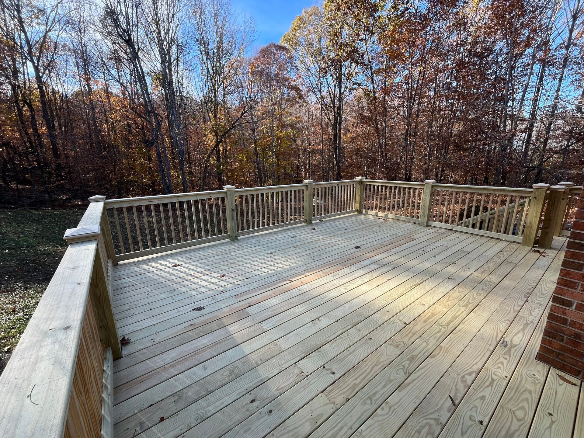 A large wooden deck with a railing and trees in the background.