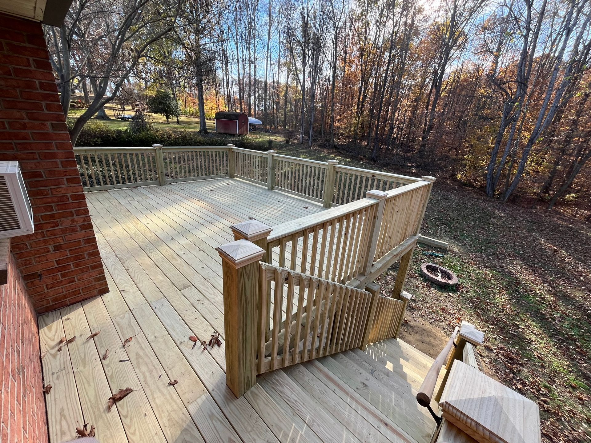 A wooden deck with a fire pit in the backyard of a house.