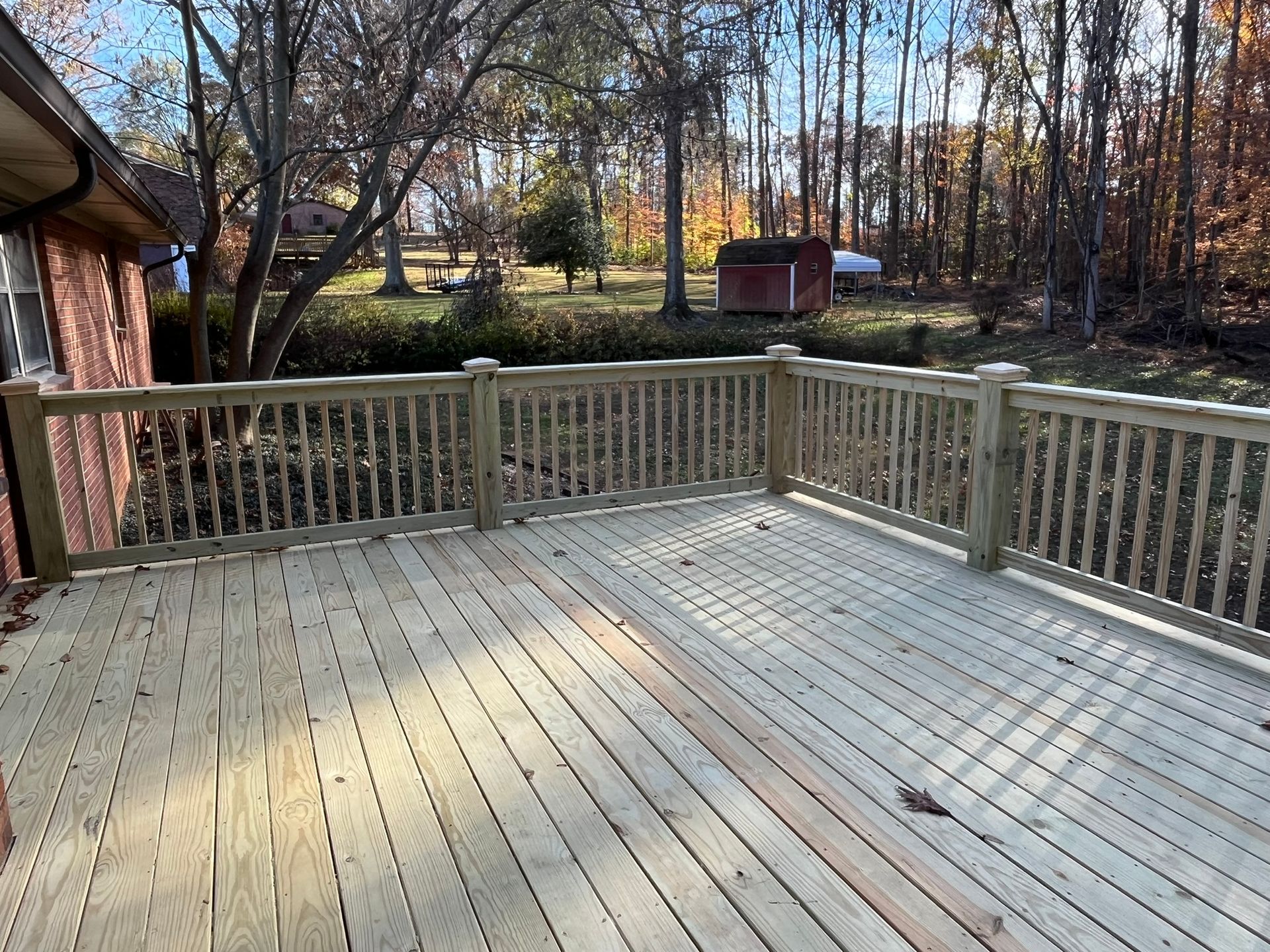 A large wooden deck with a railing and trees in the background.