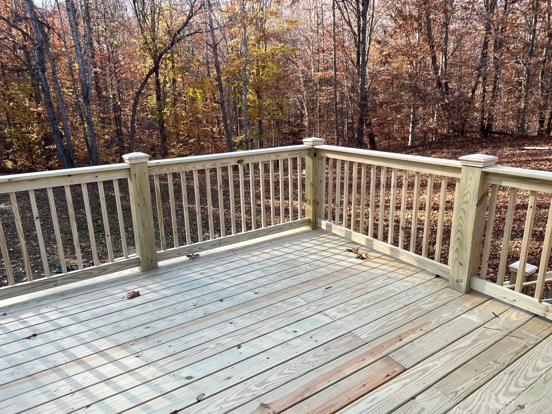 A wooden deck with a railing and trees in the background.