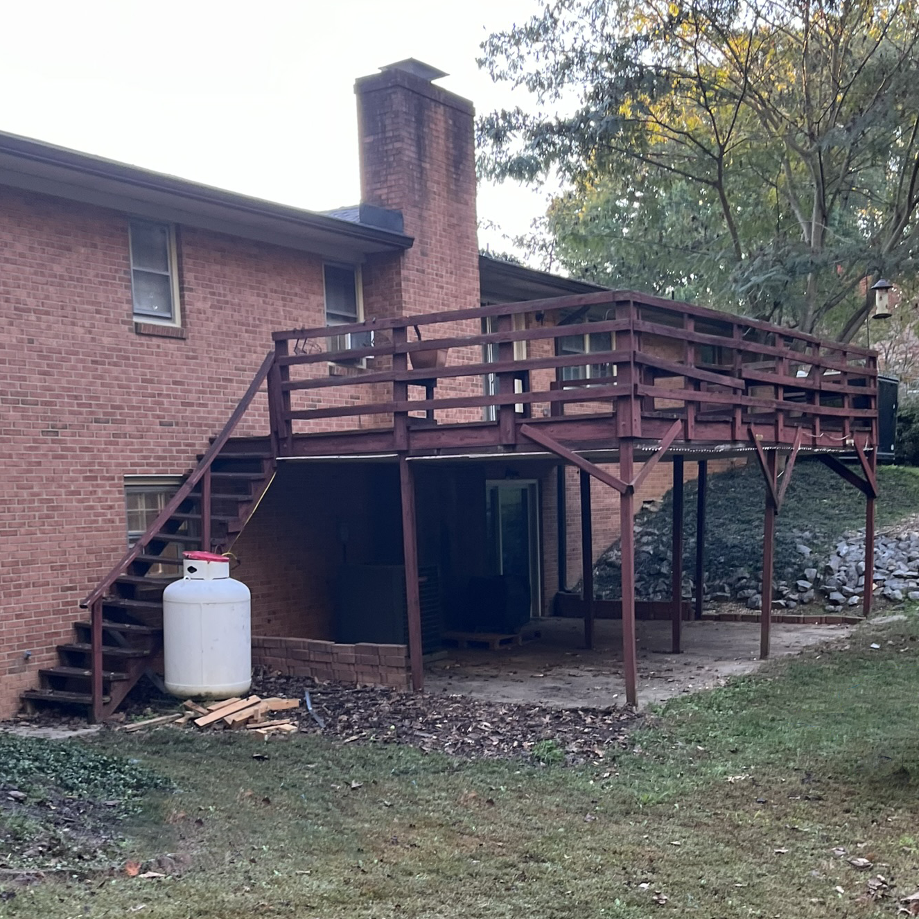A wooden deck with stairs leading up to it is in front of a brick house.