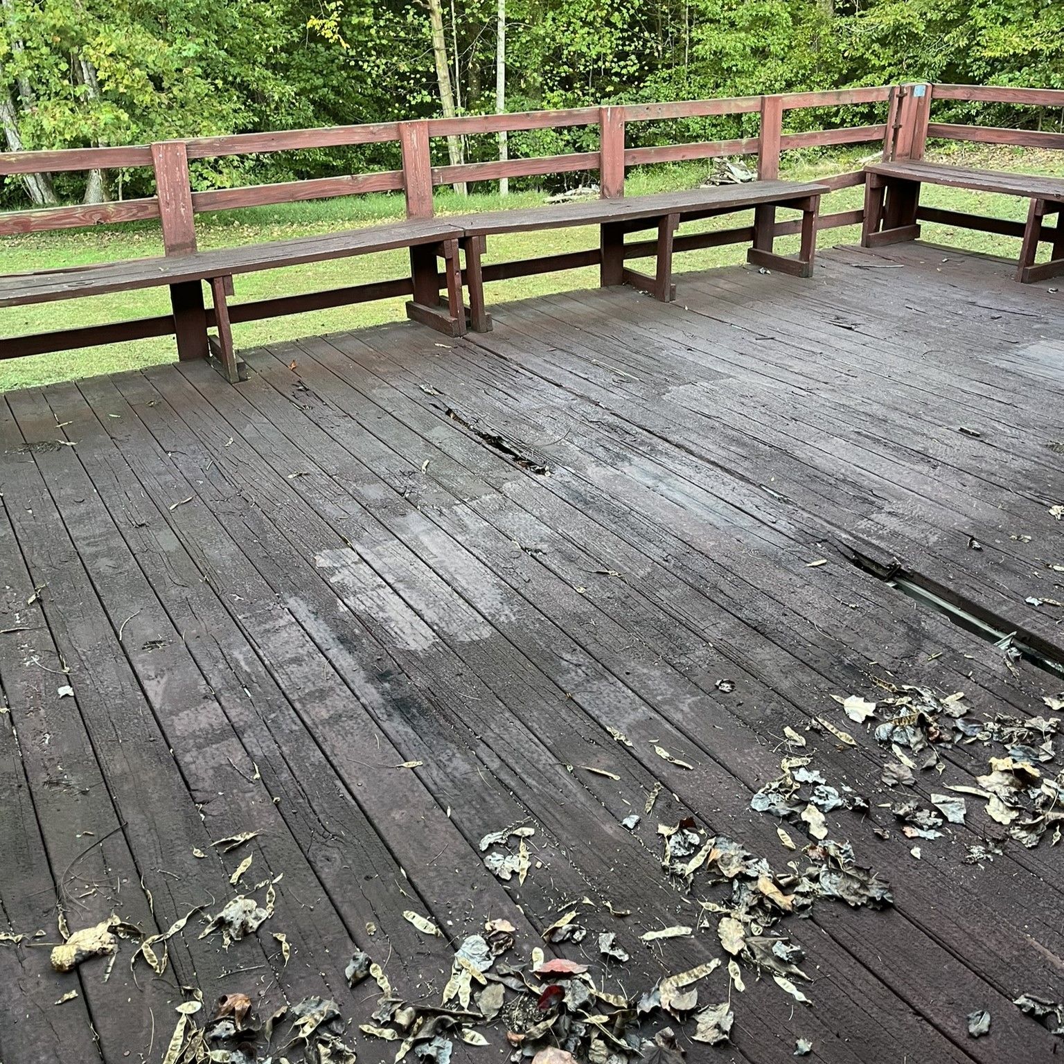A wooden deck with benches and leaves on it.