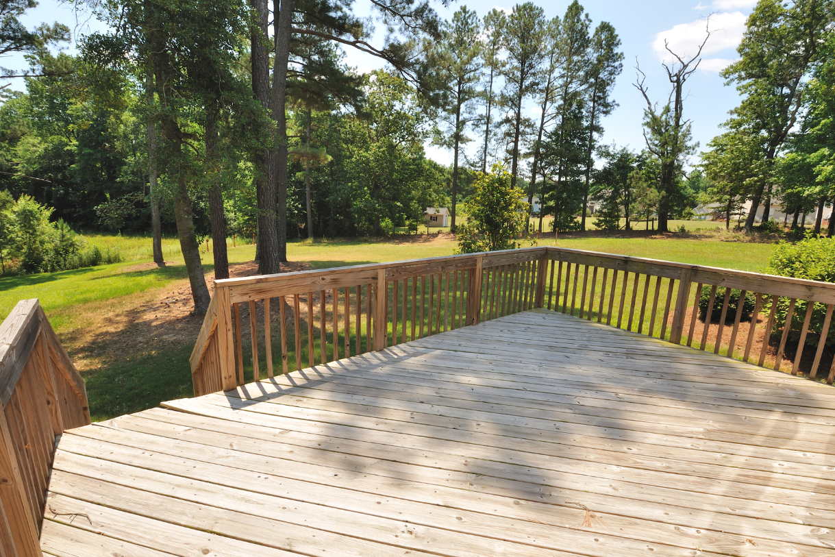 A wooden deck with a railing and trees in the background