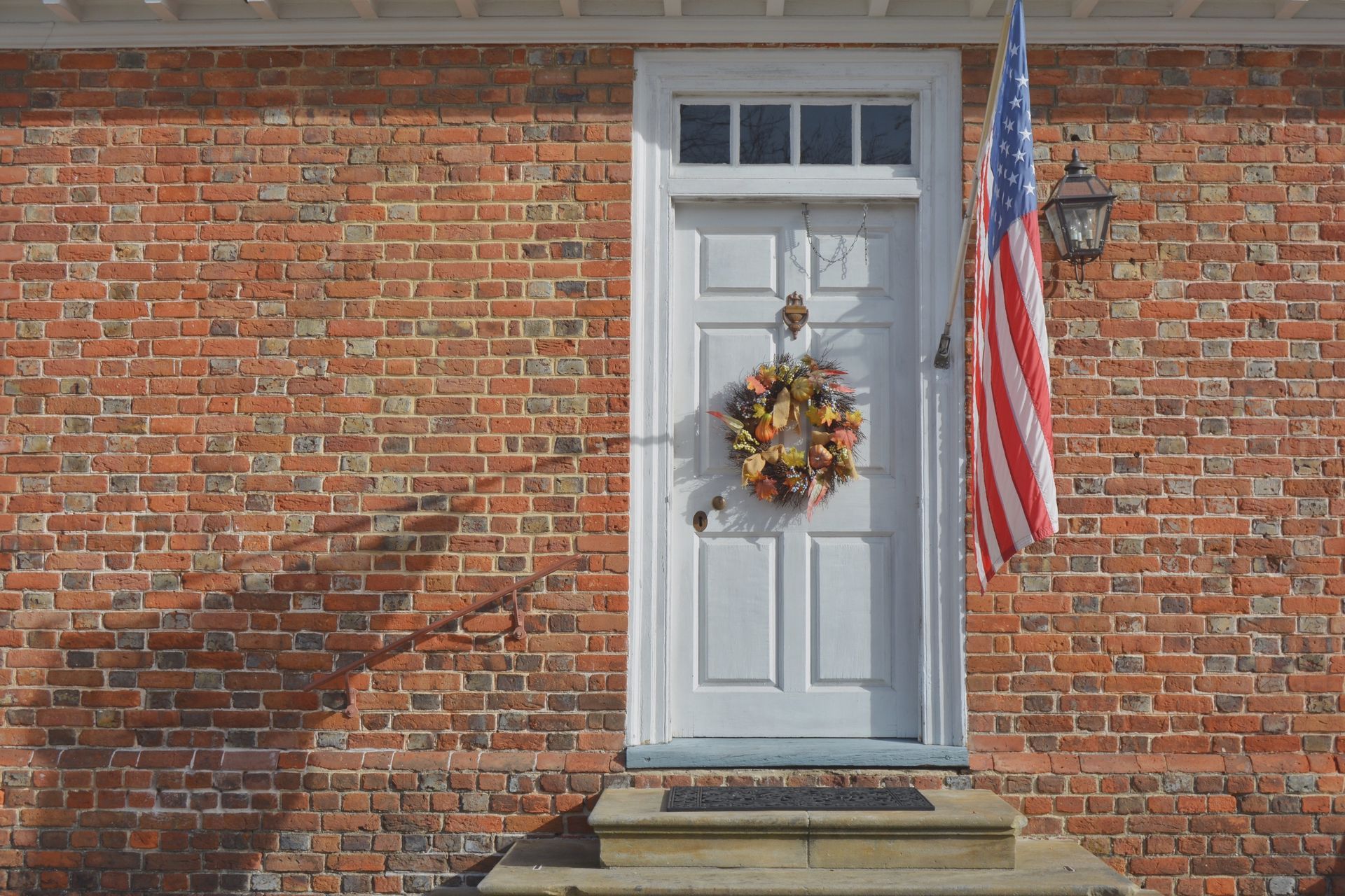A white door with an american flag hanging on it is on a brick building.