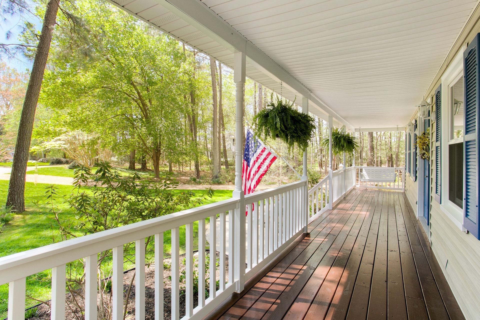 A long porch with a white railing and an american flag hanging from it.