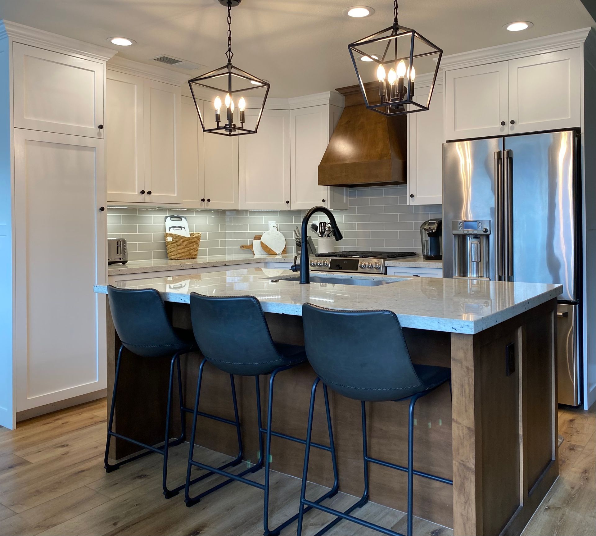 A kitchen with white cabinets , stainless steel appliances , a large island and stools.