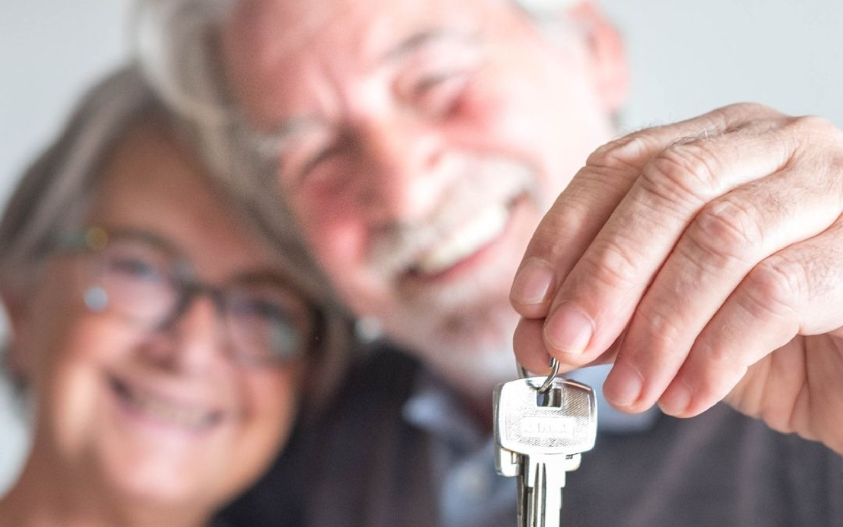 Senior couple holding house keys, smiling, in bright setting.