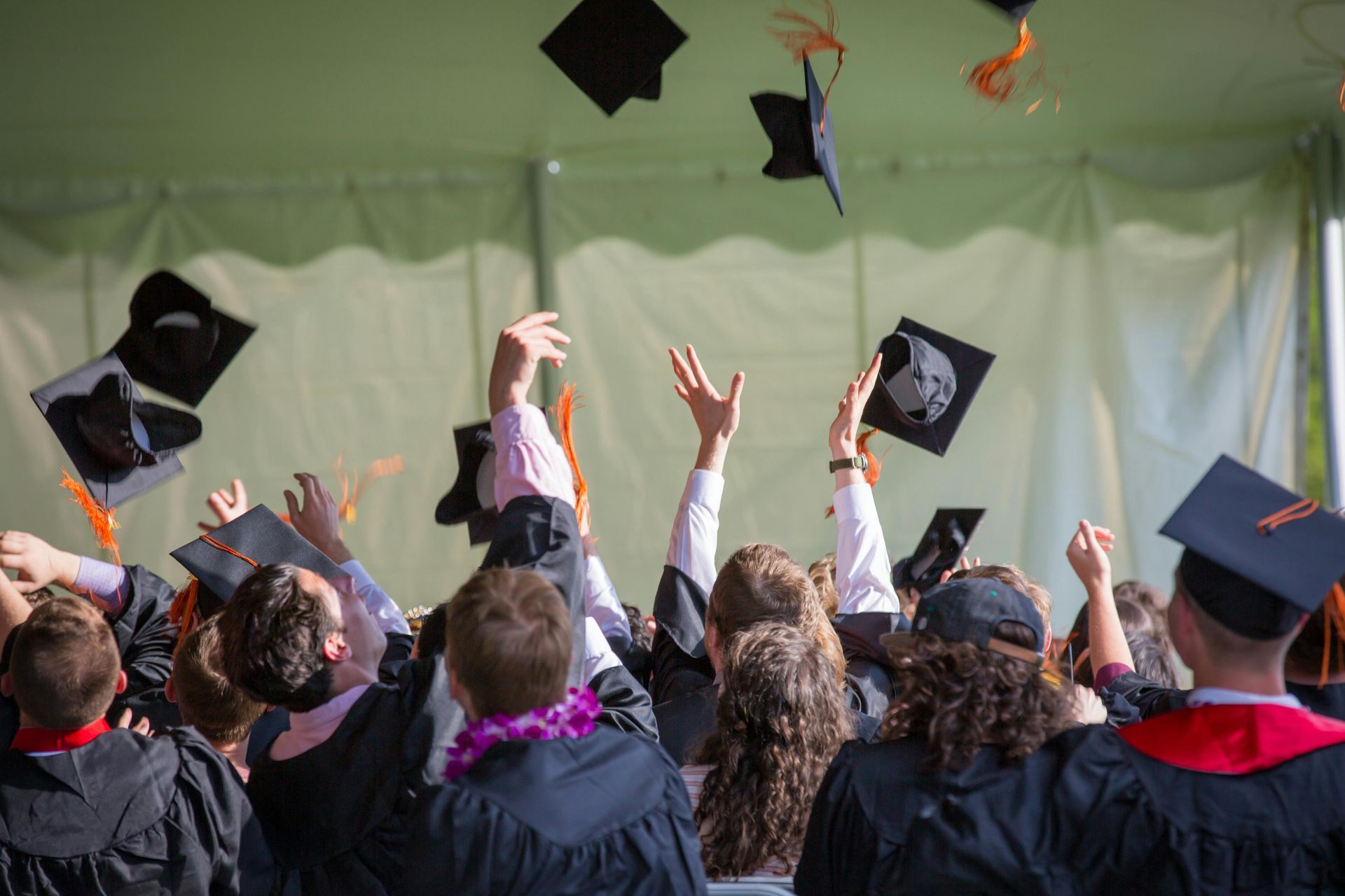 Graduates in black gowns toss graduation caps in the air during a ceremony.