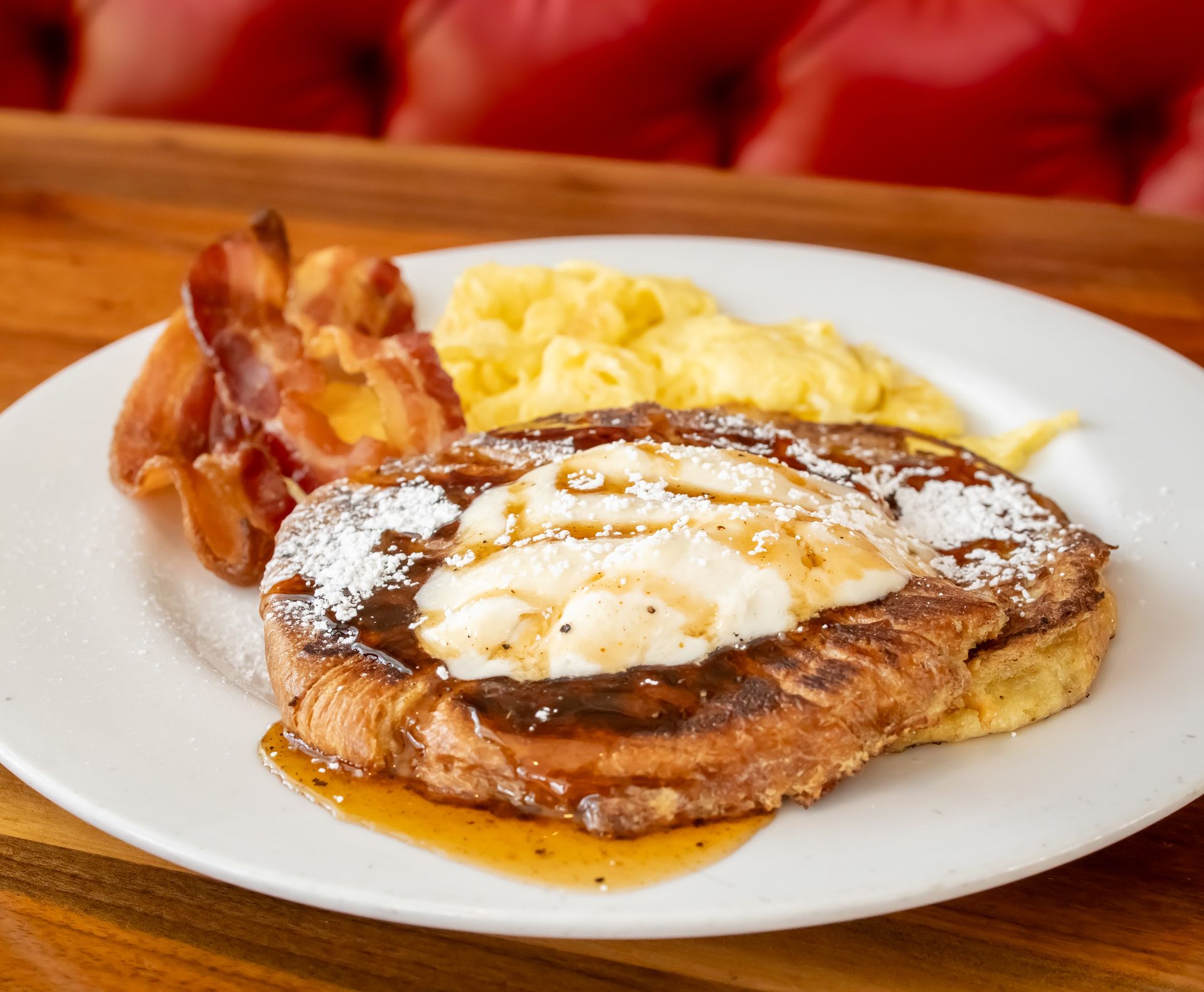A white plate topped with french toast , scrambled eggs and bacon.