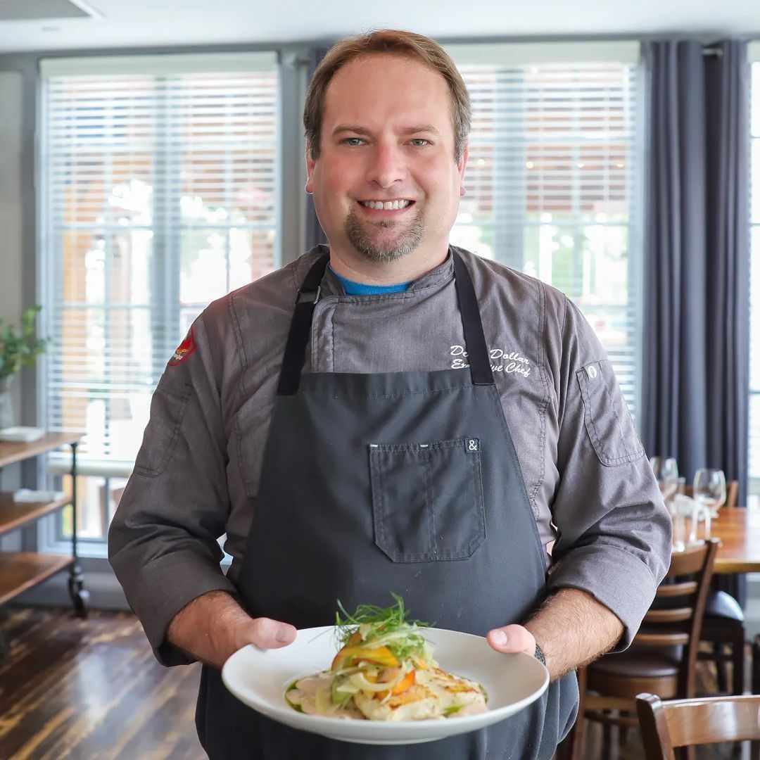 A man in an apron is holding a plate of food