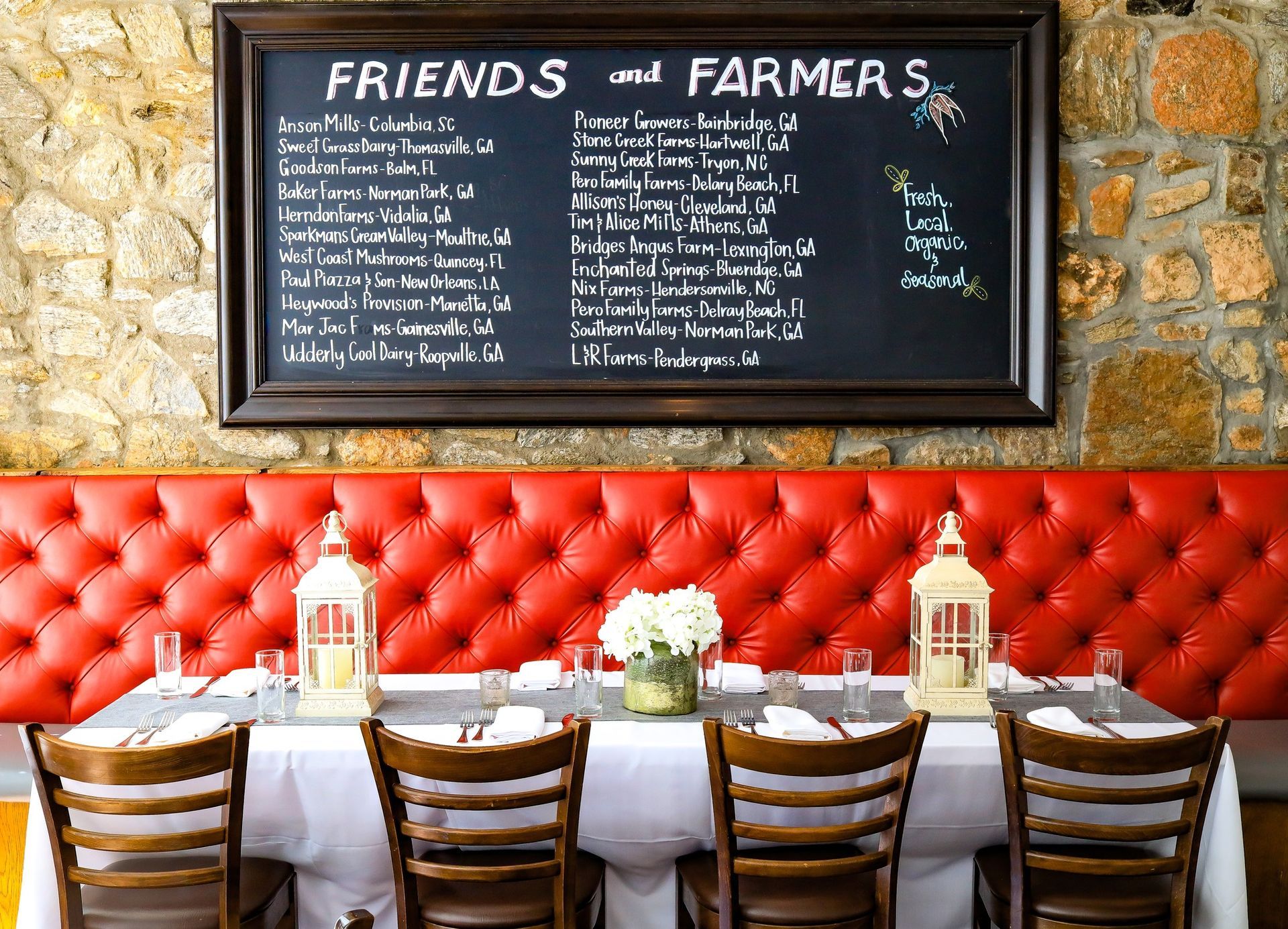 Restaurant table set for dining, red booth, chalkboard menu, stone wall.