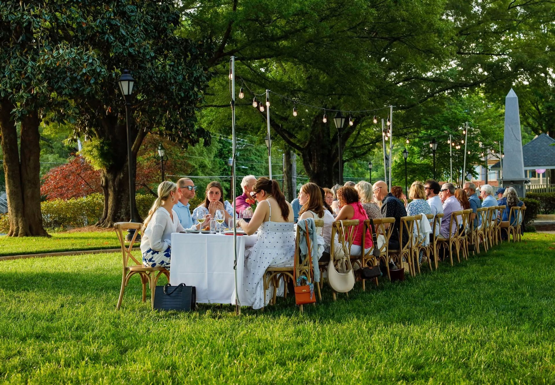 A group of people are sitting at long tables in a park.