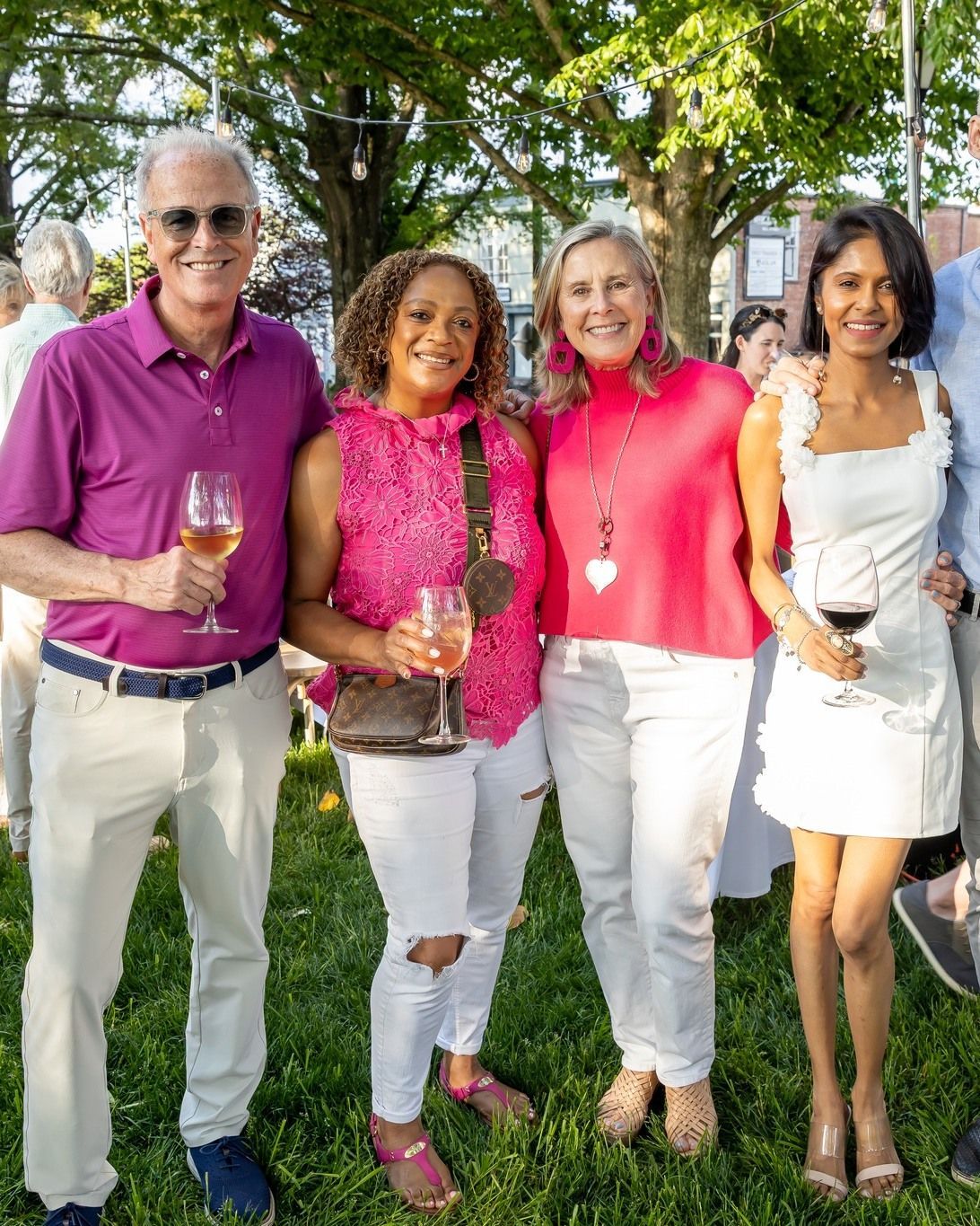 A group of people standing next to each other in the grass holding wine glasses.