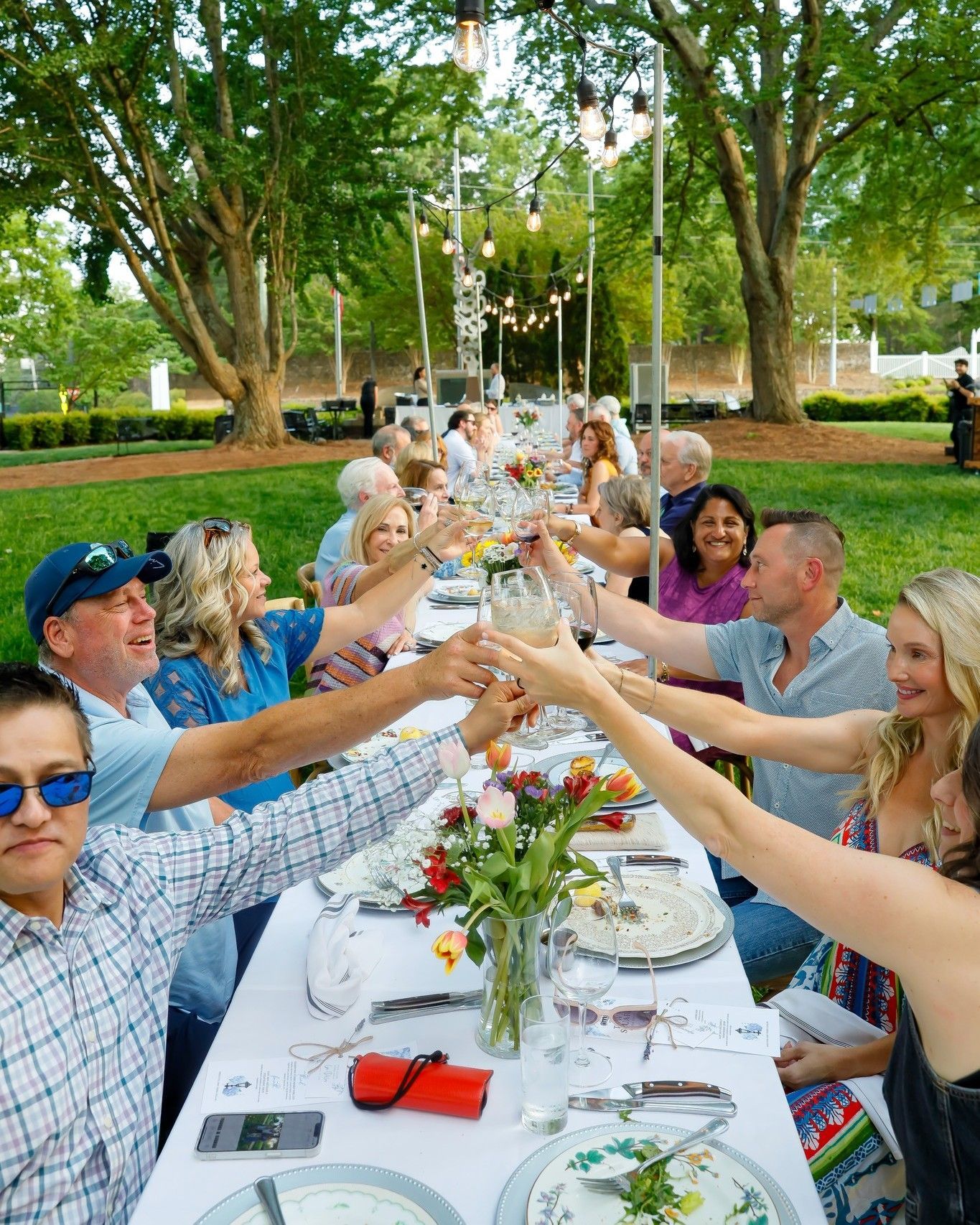 A group of people are sitting at a long table toasting with their hands.