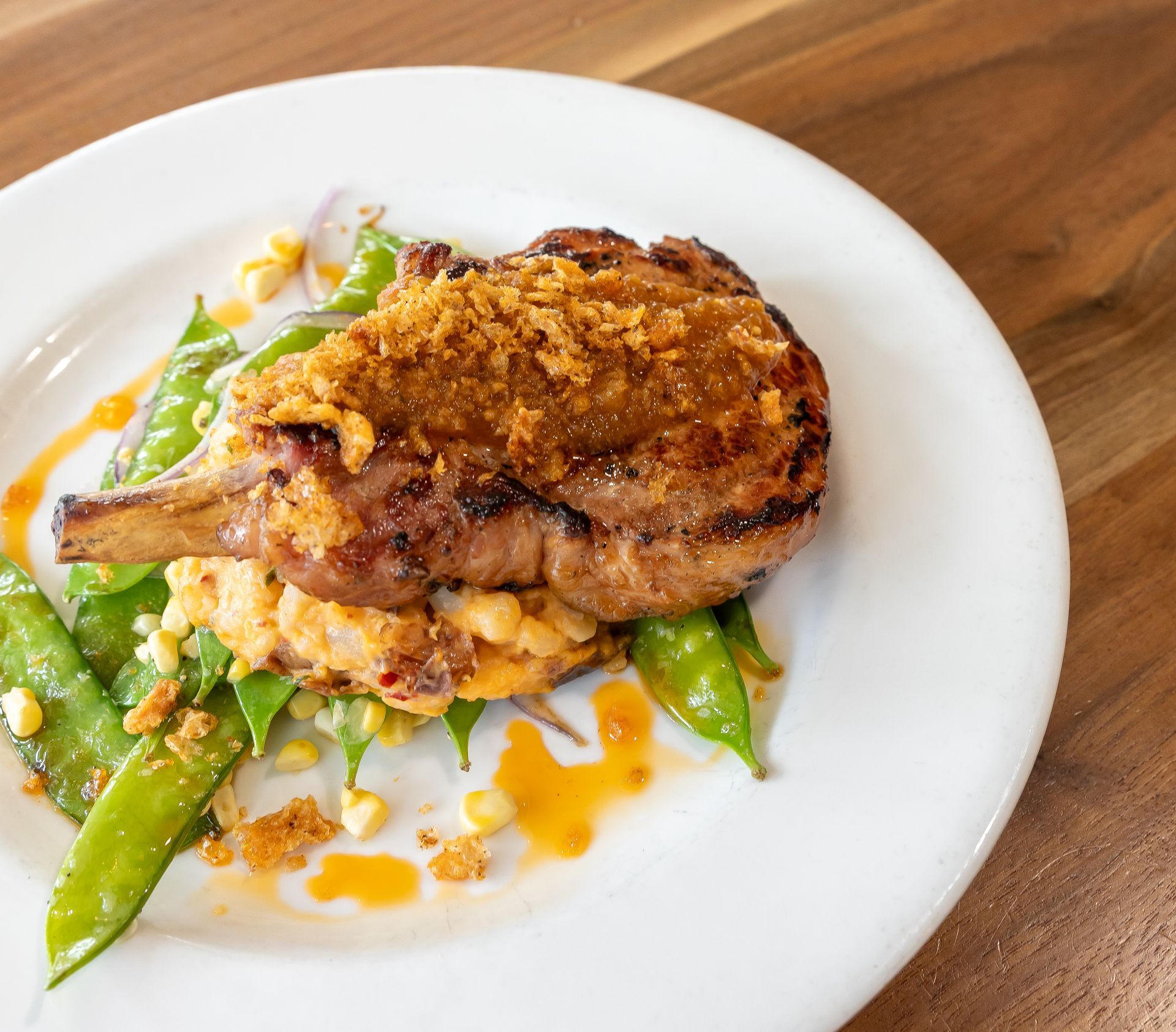 A white plate topped with meat and vegetables on a wooden table