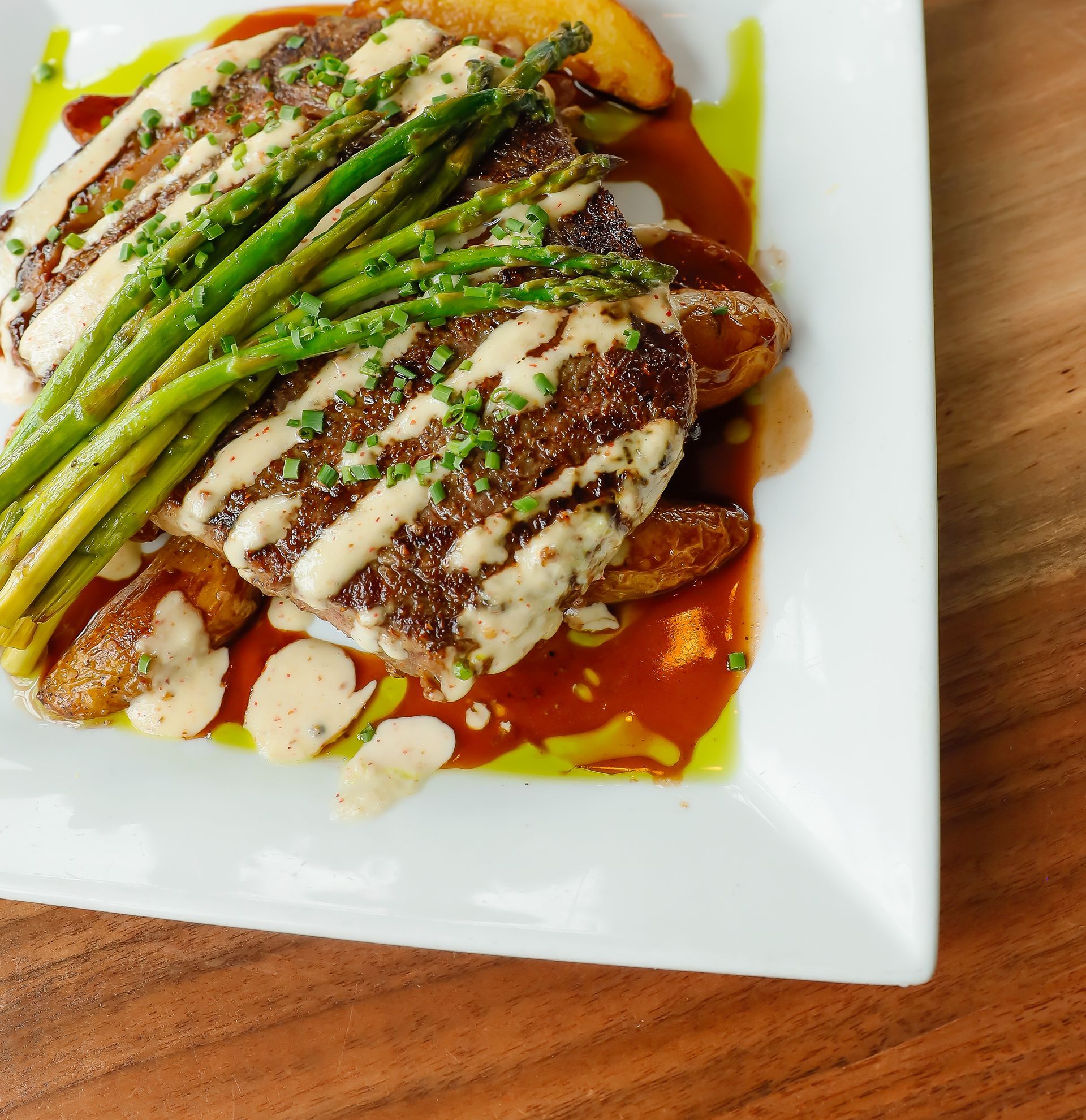 A white plate topped with meat and asparagus on a wooden table