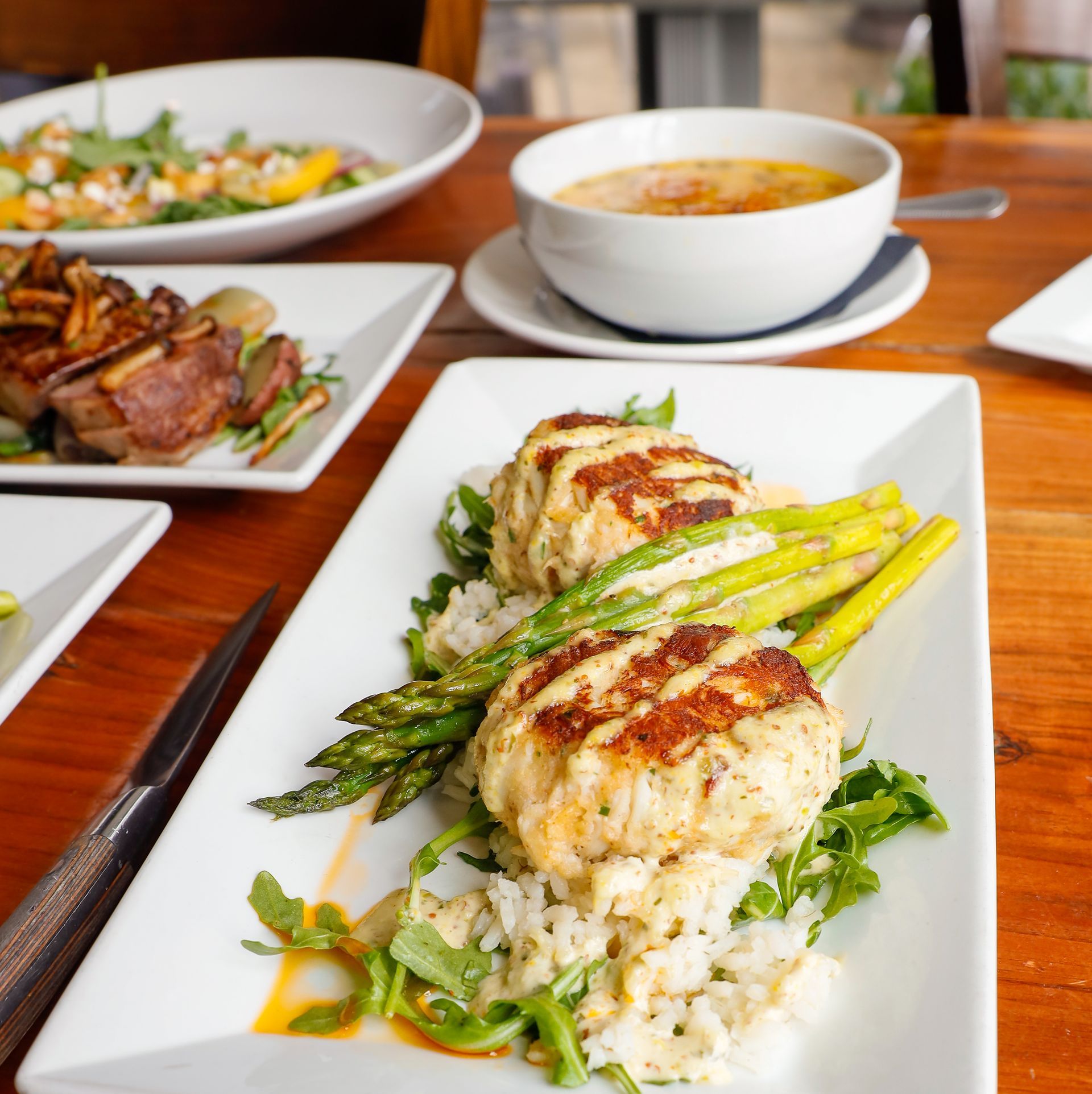 A wooden table topped with plates of food and a bowl of soup