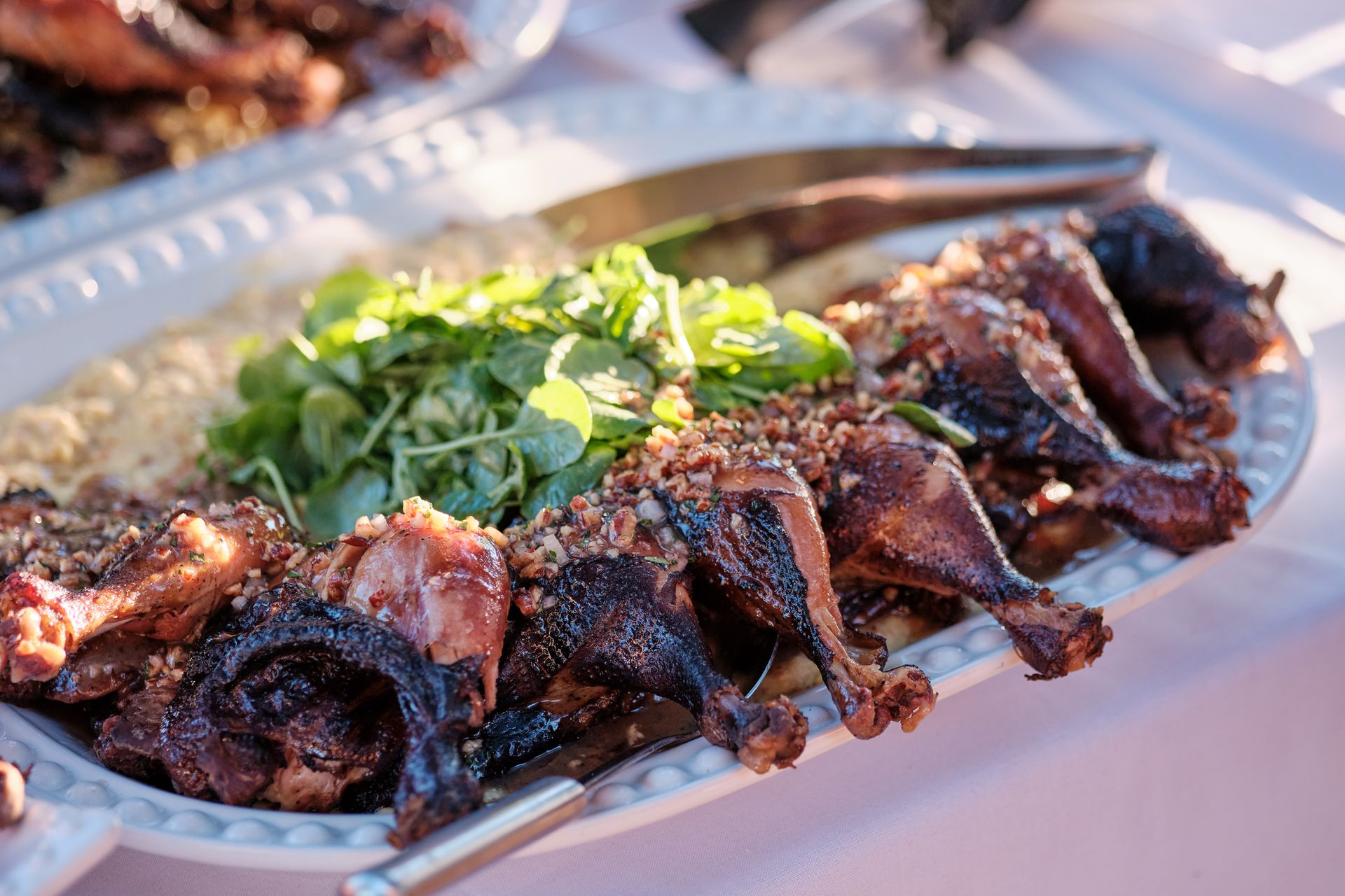 Platter of dark roasted game hens with side of greens and creamy dip.
