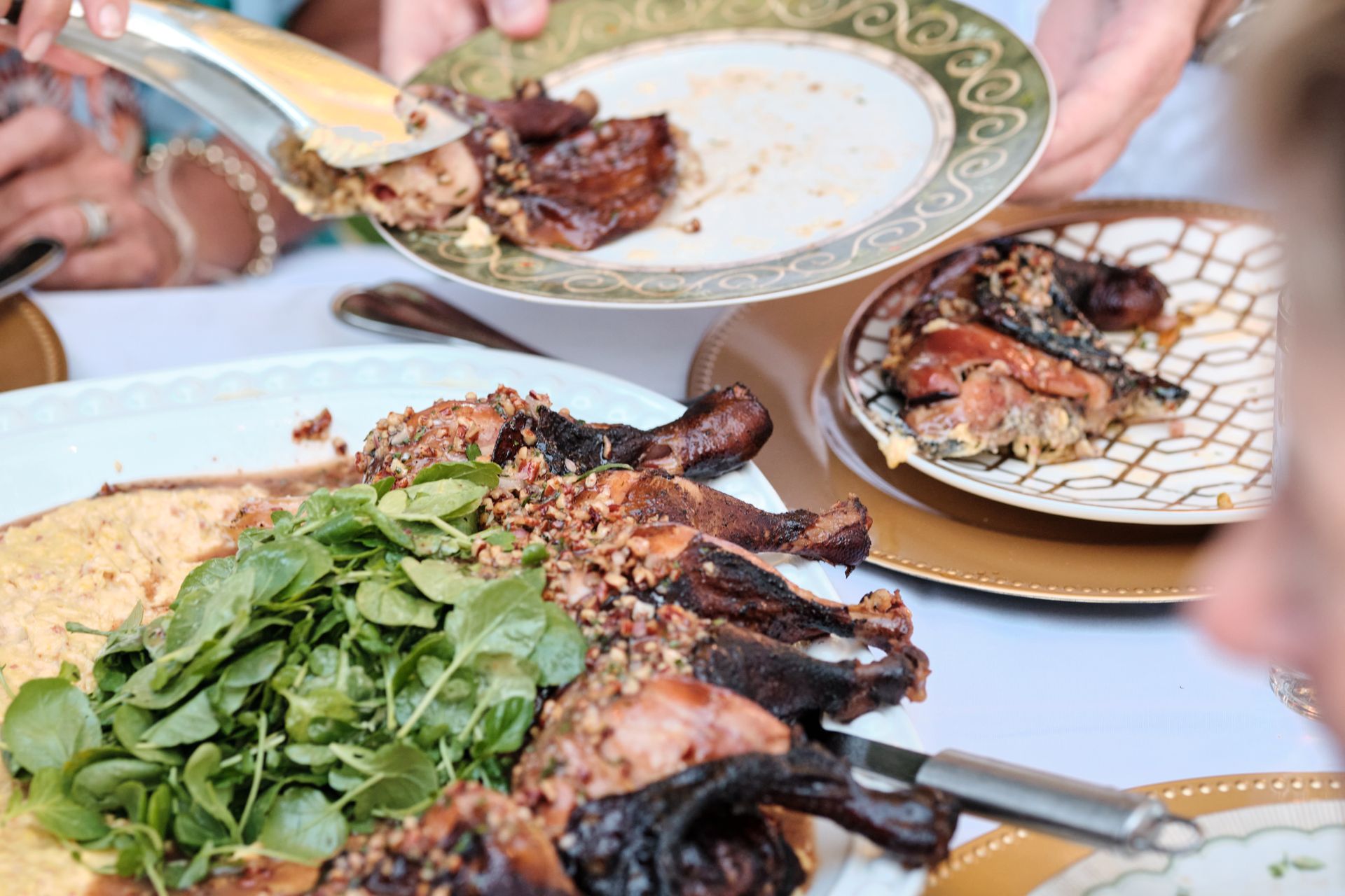 People serving and eating roasted meat with greens and cornbread at a table.