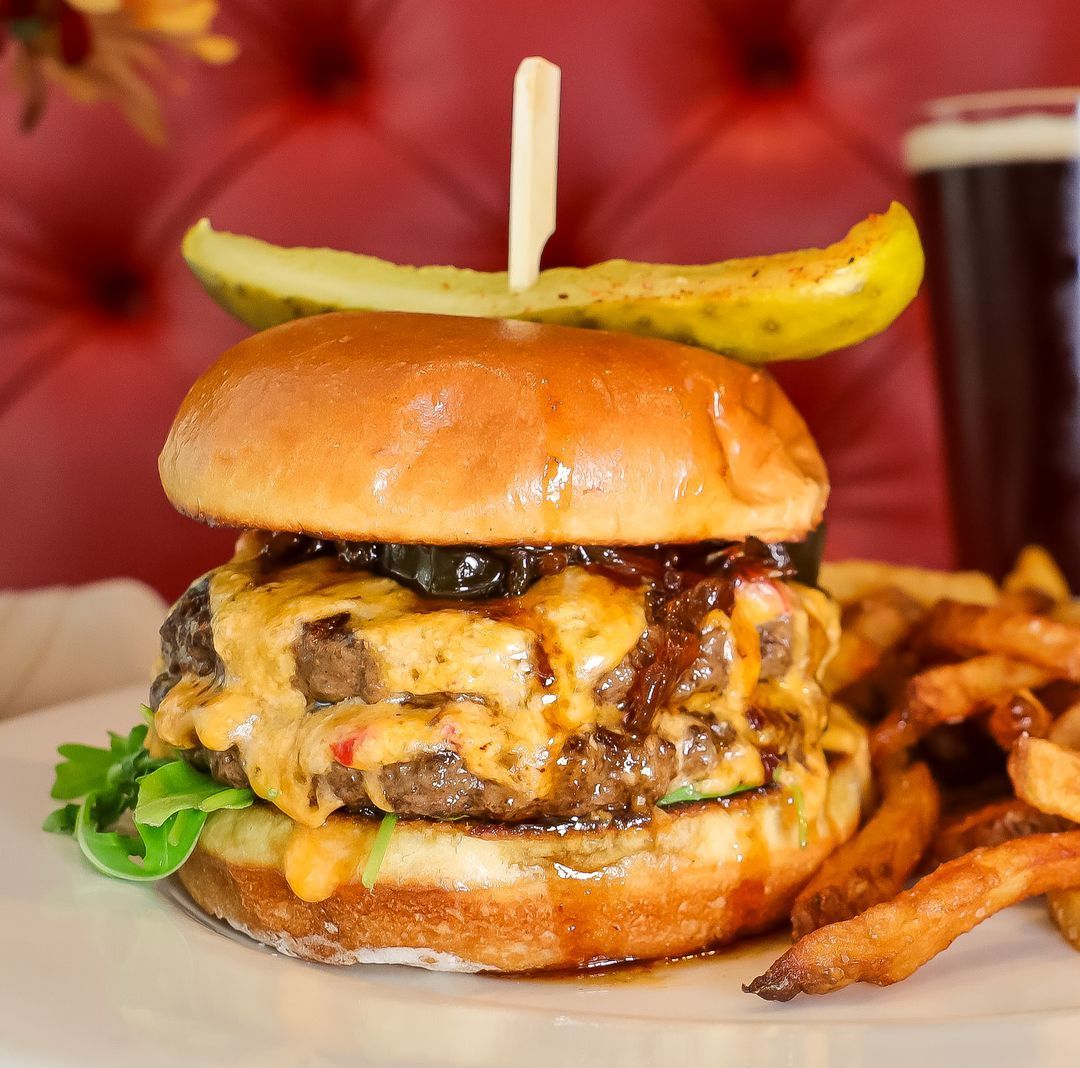 A hamburger with a pickle on top of it and french fries on a plate.