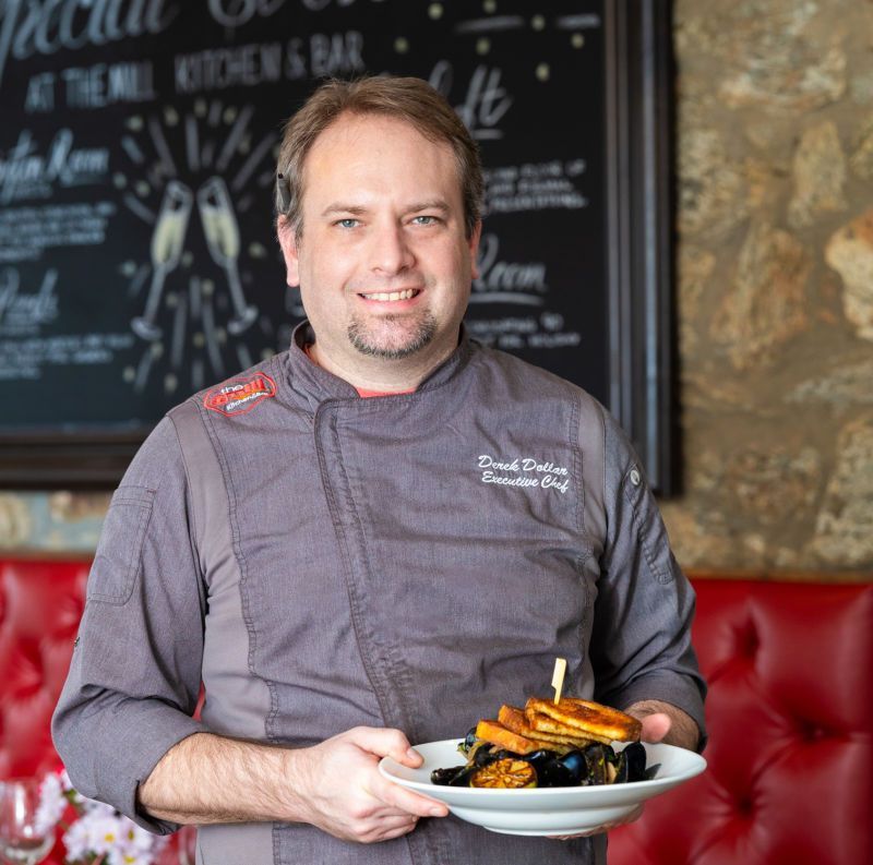 A man in a chef 's uniform is holding a plate of food