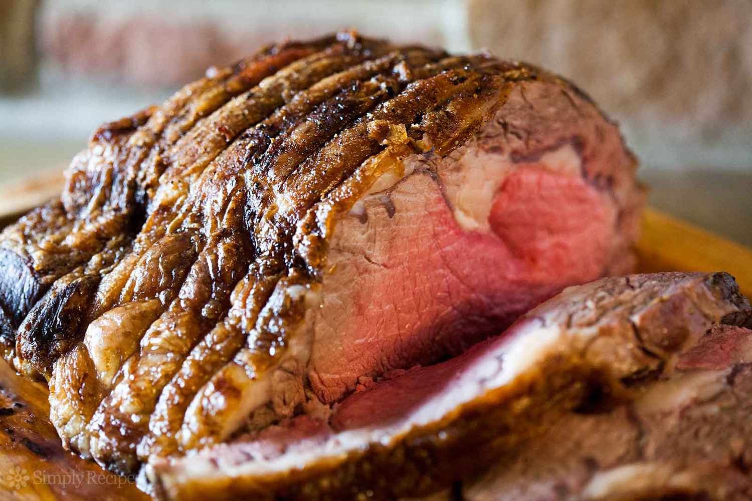 A large piece of prime rib is sitting on top of a wooden cutting board.