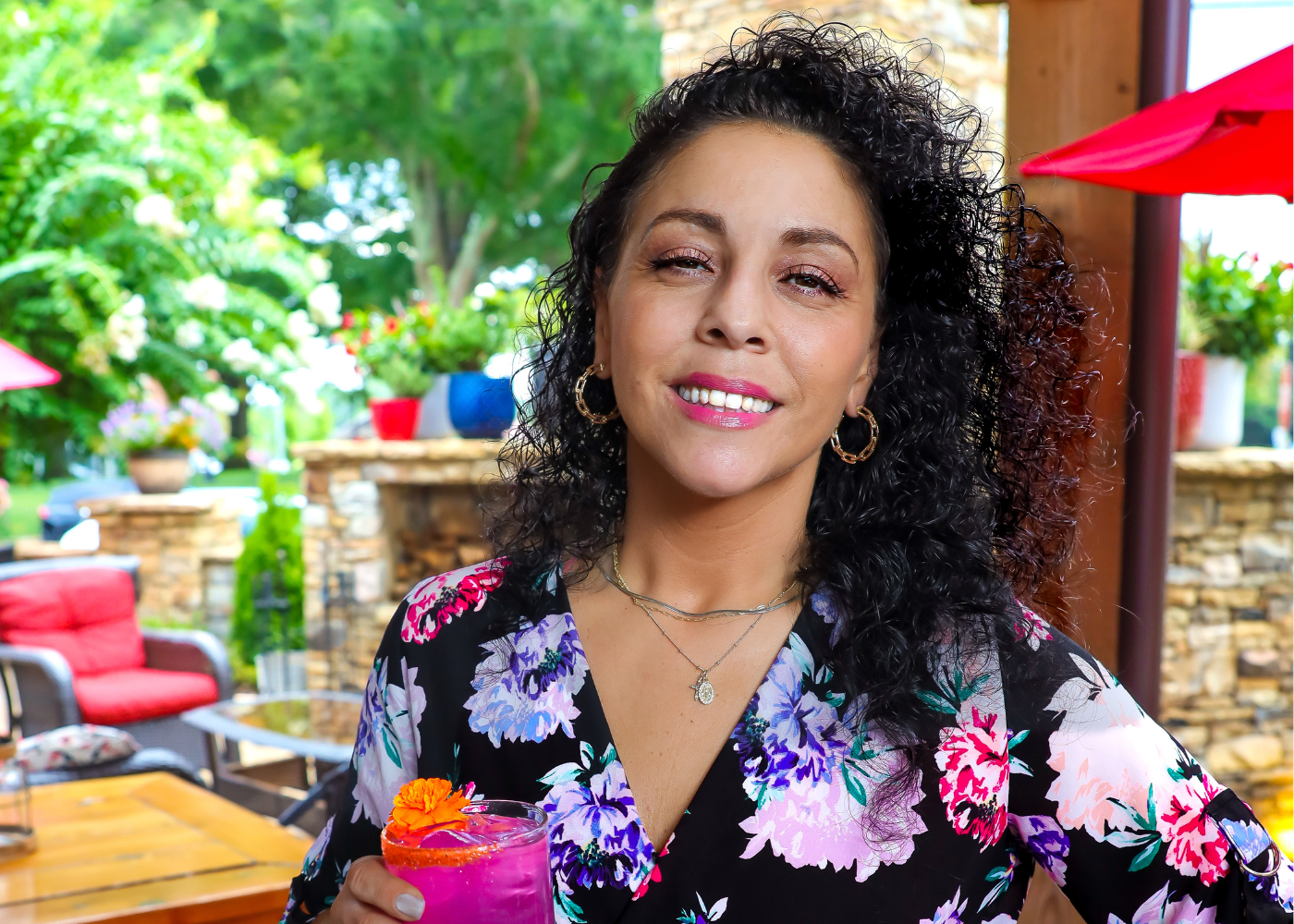 A woman in a floral shirt is holding a purple drink.
